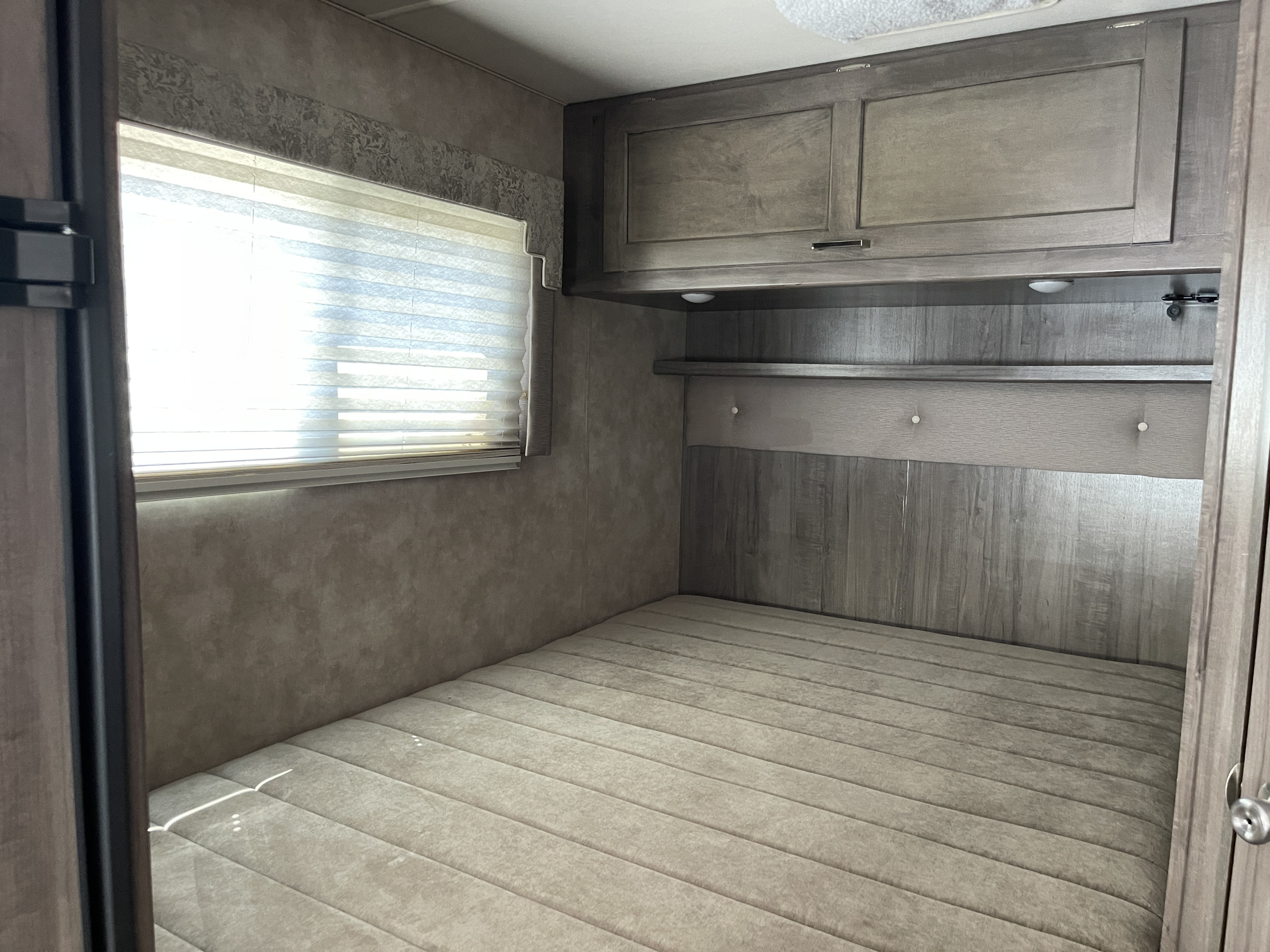 This cozy RV rental bedroom features a comfortable bed, a bright window with blinds, and practical overhead cabinets.. Winnebago Minnie Winnie 2019