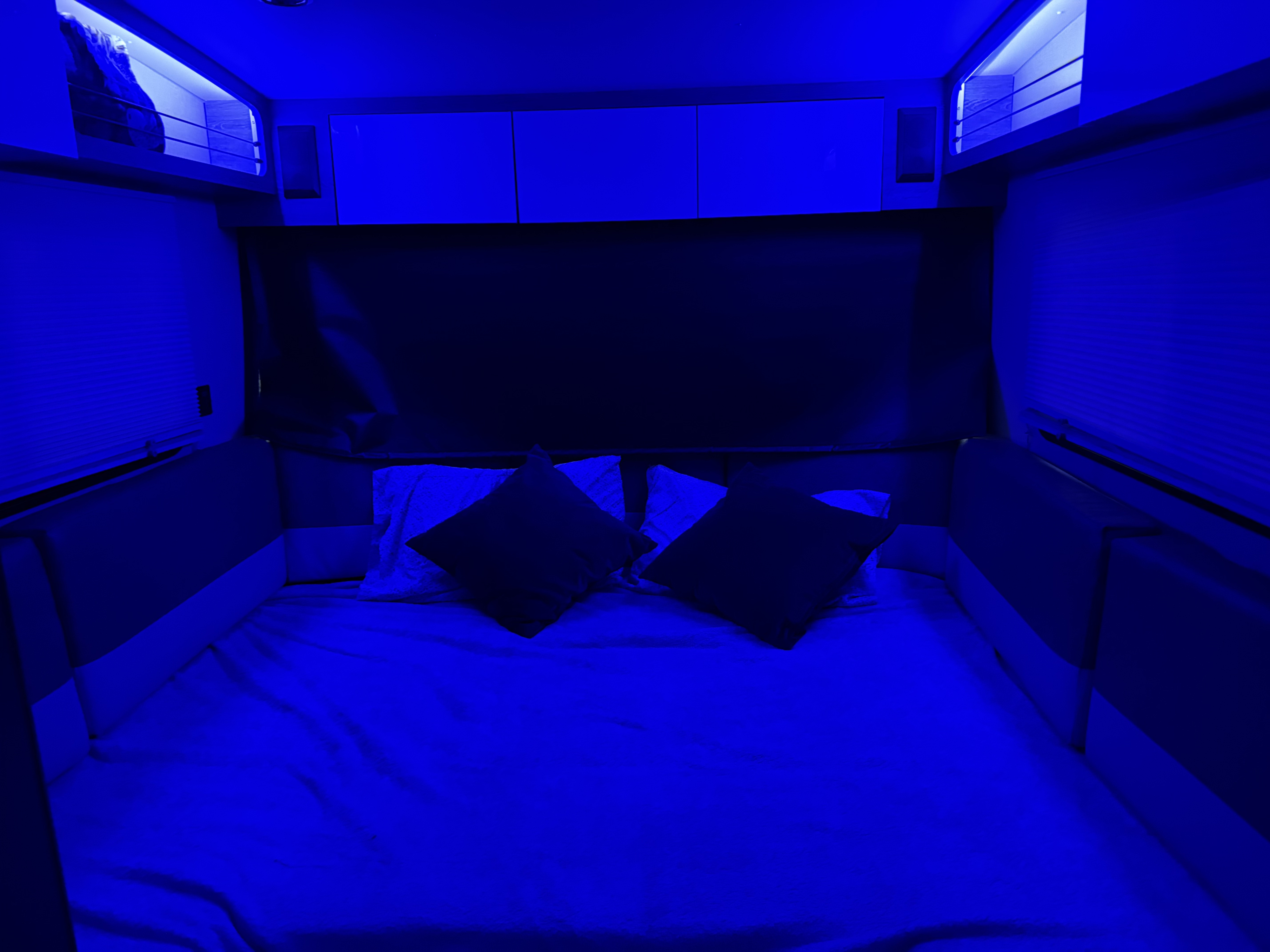 RV rental bedroom: a cozy blue-lit space with a bed, overhead storage, and privacy blinds.. InTech RV SOL 2021