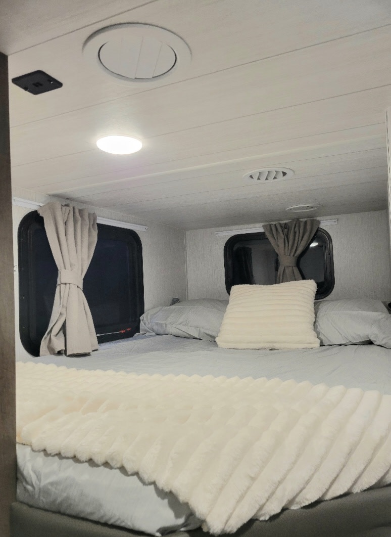 Cozy RV rental bedroom with comfortable bed, soft bedding, and natural light from windows. Perfect for travel.. Forest River Bunkhouse 2022