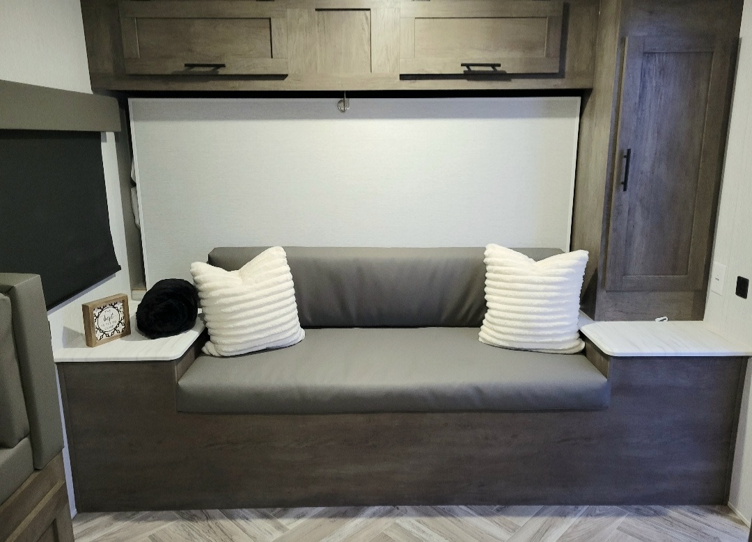 Comfortable RV rental interior with modern gray sofa, white pillows, and wood accents.. Forest River Bunkhouse 2022
