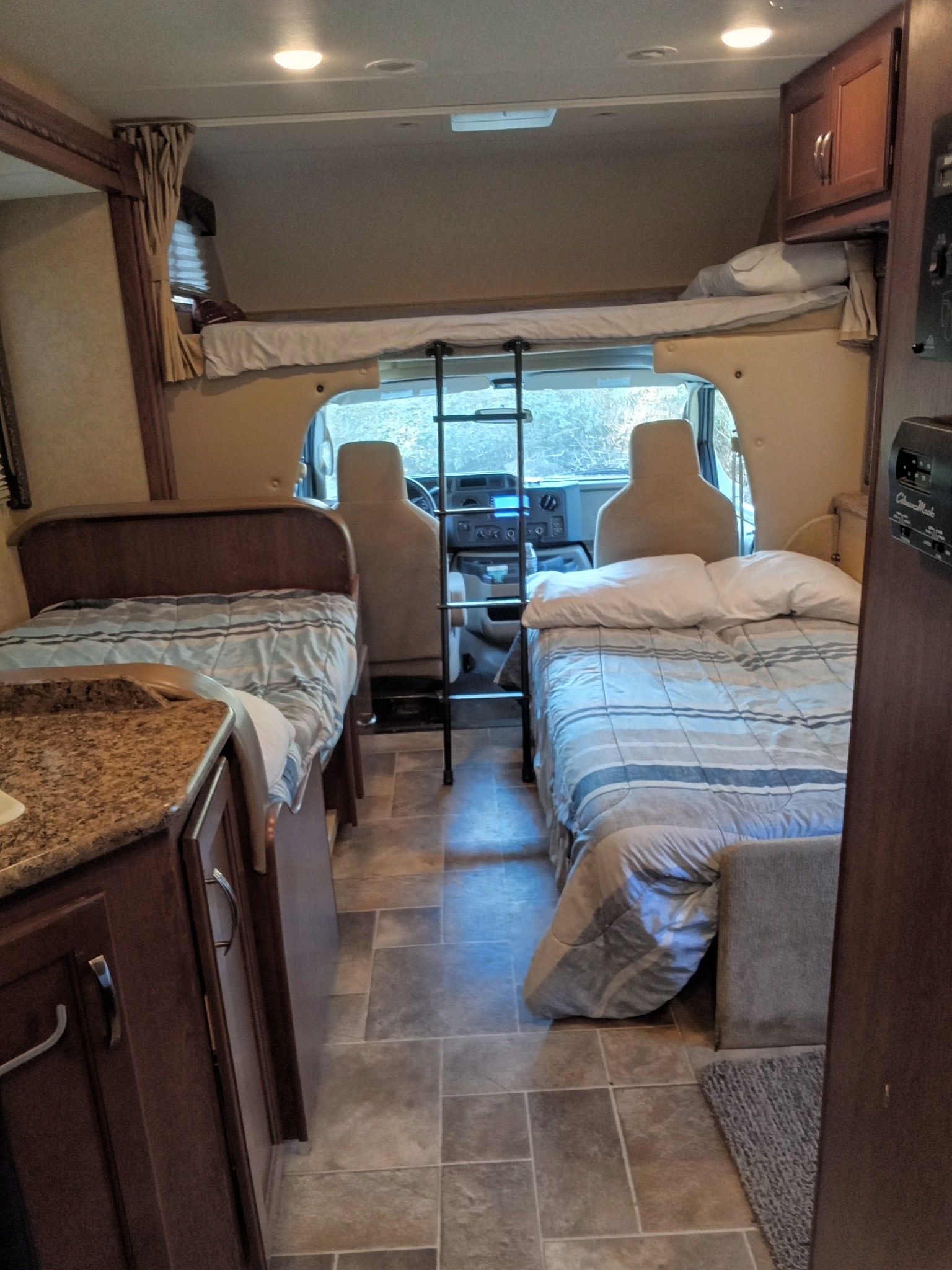 This RV rental interior features two beds, an overhead bunk, and a kitchen counter, showcasing a comfortable living space.. Thor Freedom Elite 2016