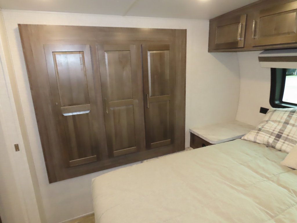 RV rental bedroom with a comfortable bed, overhead cabinets, and a large wooden storage unit on the left wall.. Forest River Rockwood Mini Lite 2023