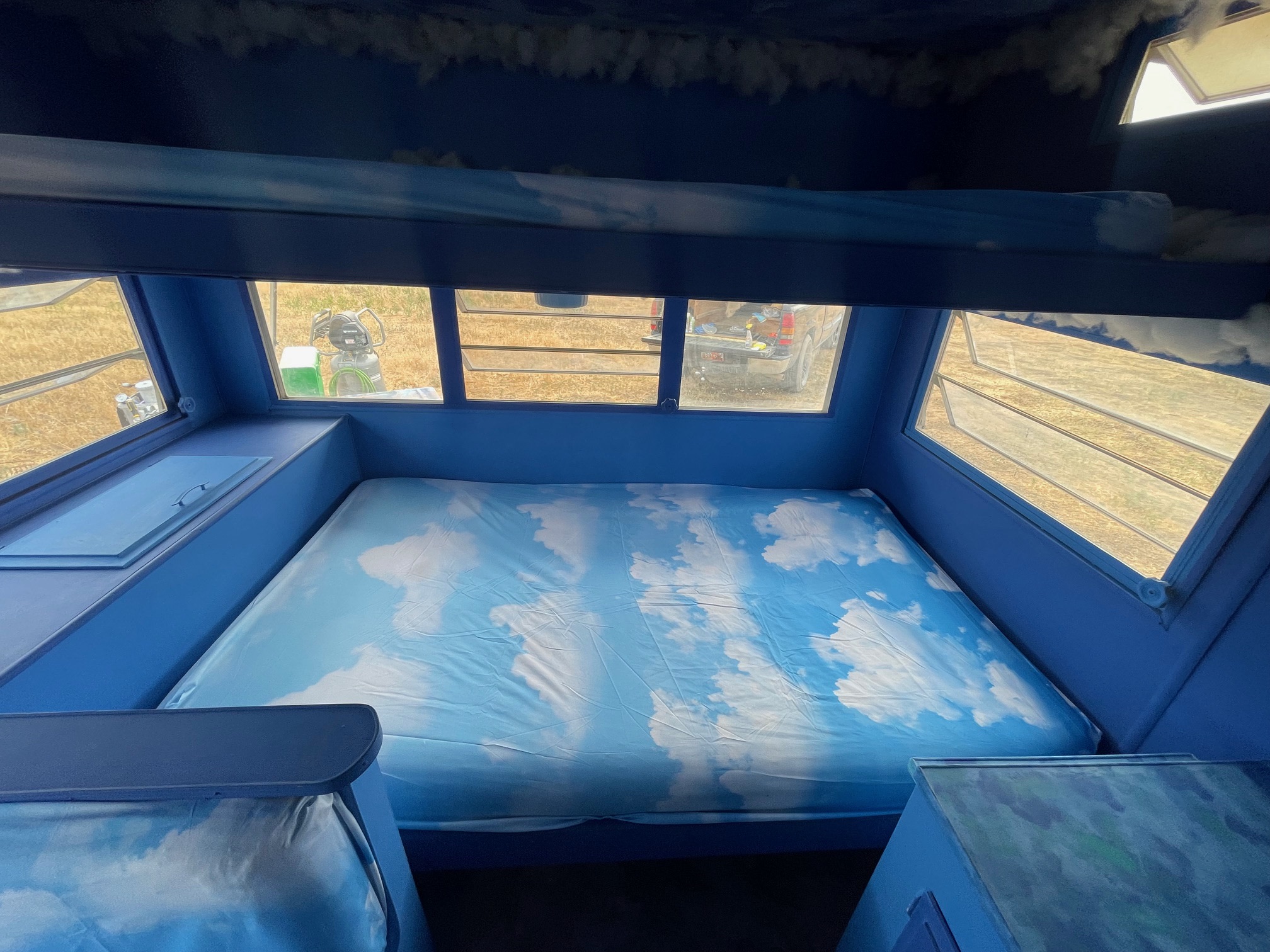 Sky-themed RV rental interior featuring a cloud bed, bunk, and windows with outdoor views.. Warn The West Puffy The Cloud EDC & Burning Man Trailer Rental 2024