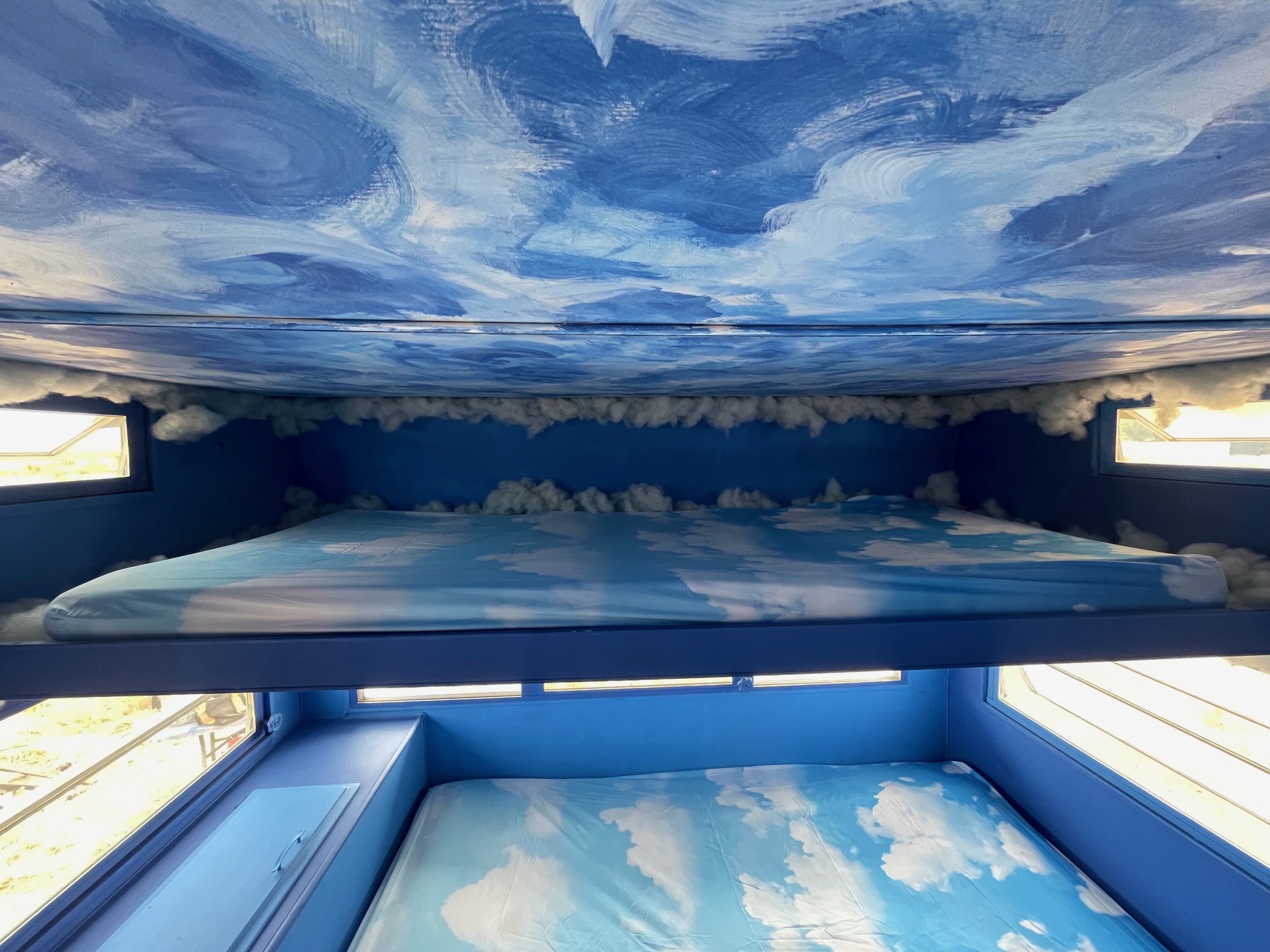 RV rental's sky-themed bunk beds. Blue interior with a painted cloud ceiling, cotton cloud borders, & patterned sheets.. Warn The West Puffy The Cloud EDC & Burning Man Trailer Rental 2024