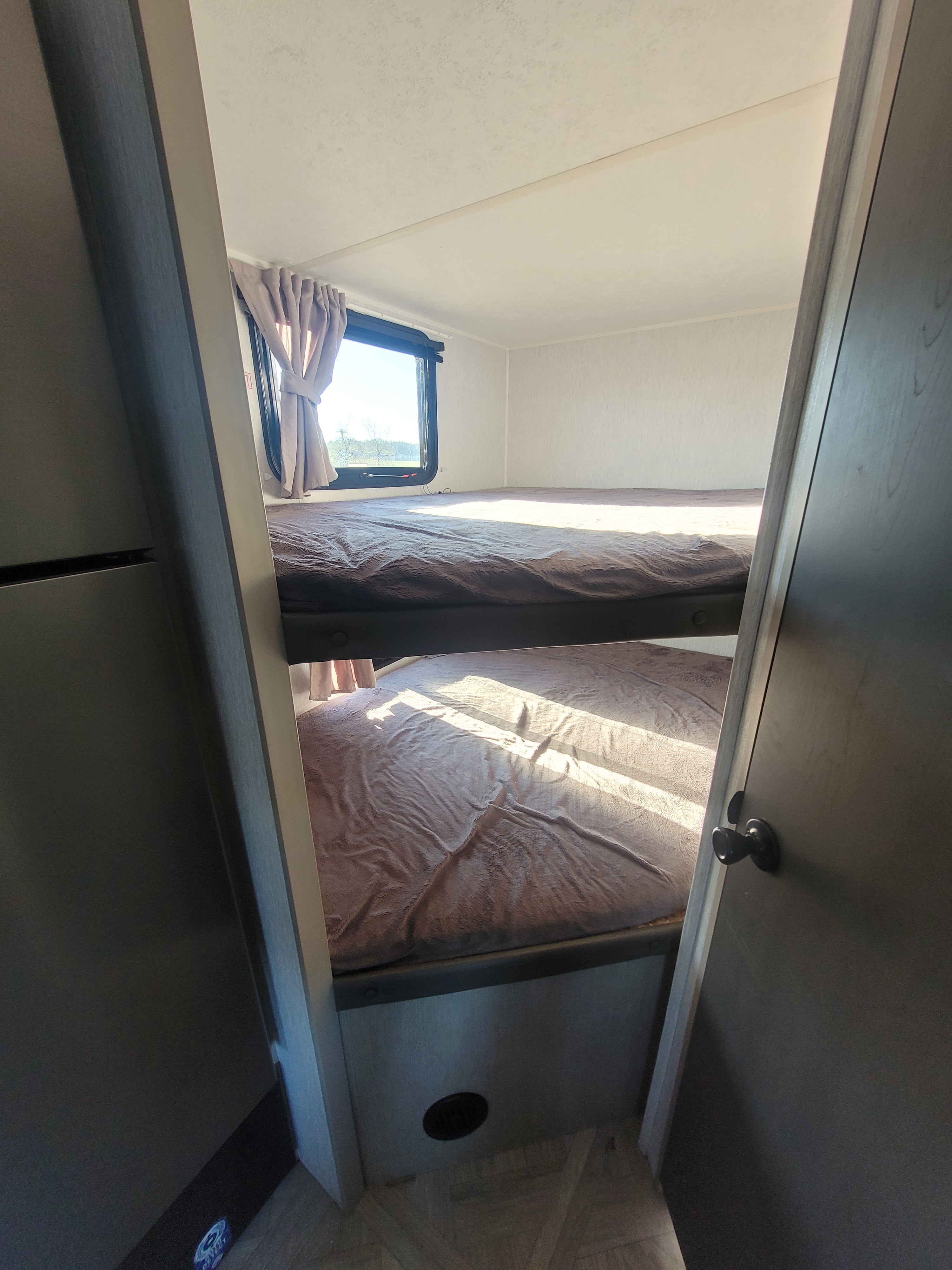 Cozy RV rental interior featuring two comfortable bunk beds bathed in sunlight from the window. Ideal for family travel.. Forest River Salem Cruise Lite 2023