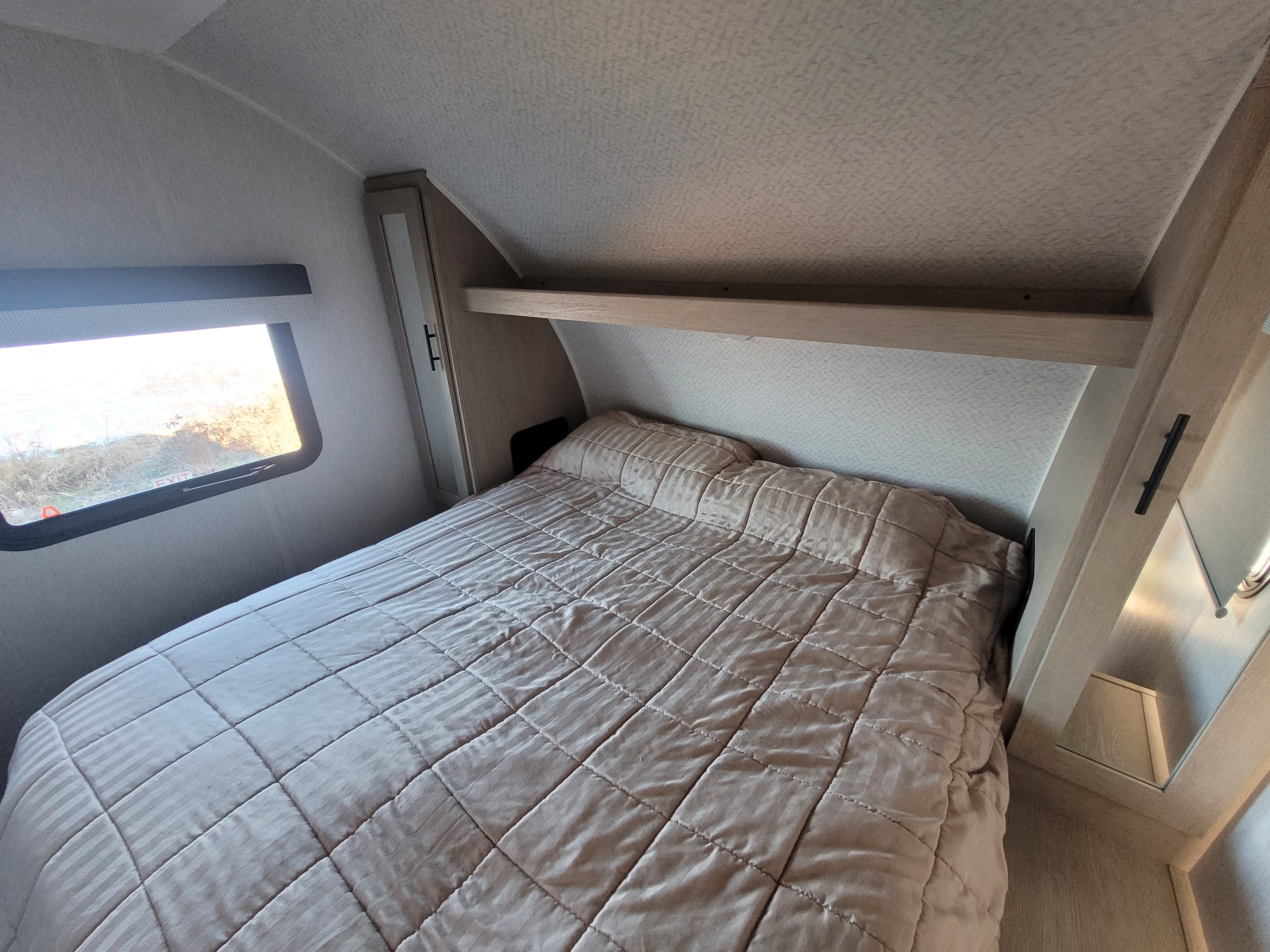 Inside an RV rental: a cozy bedroom featuring a quilted bed, window, and convenient overhead storage.. Forest River Salem Cruise Lite 2023