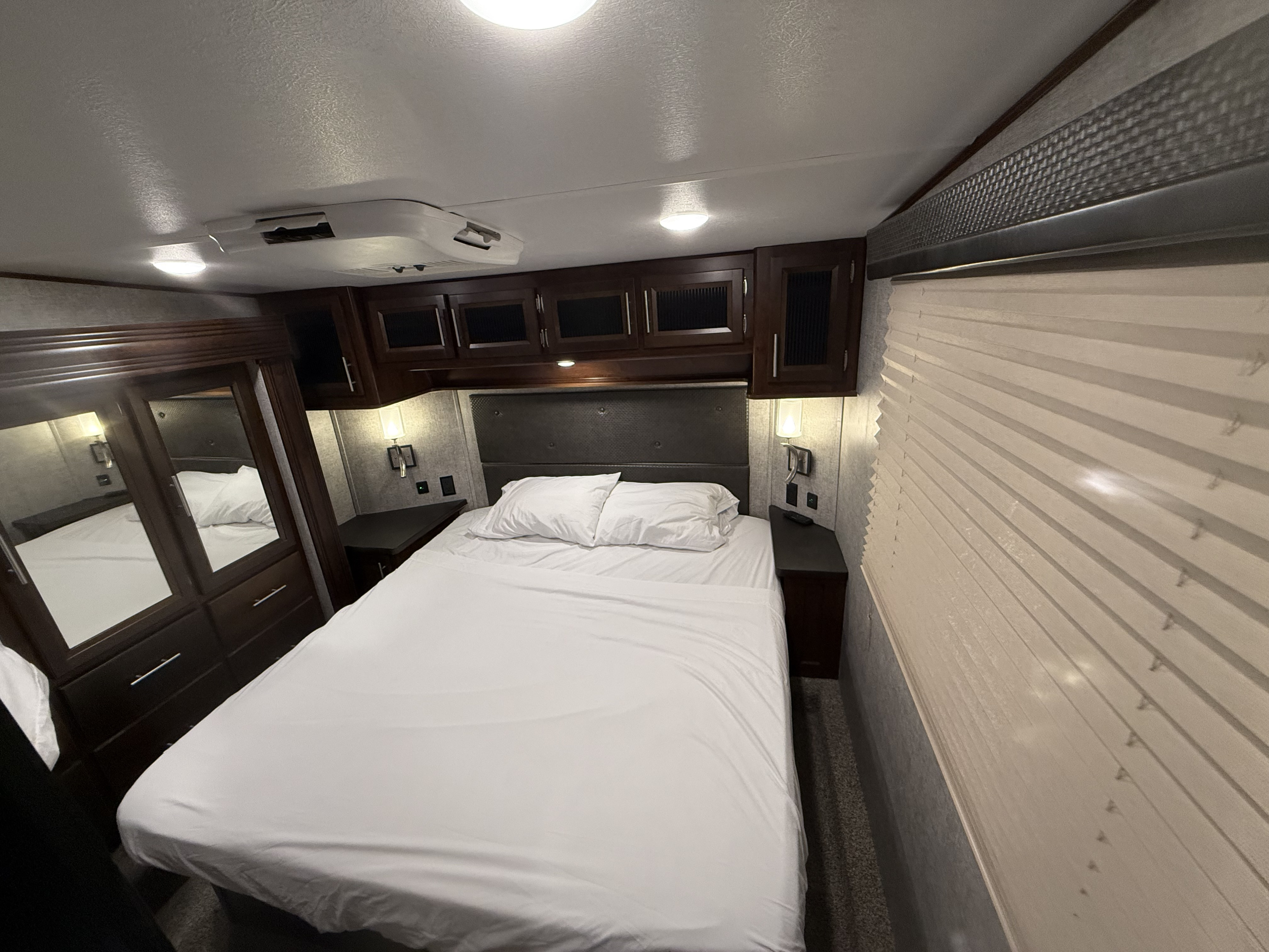 Comfortable RV rental bedroom showcasing a cozy bed, dark wood cabinets, and an overhead AC unit.. Forest River Vengeance Toy Hauler 2019