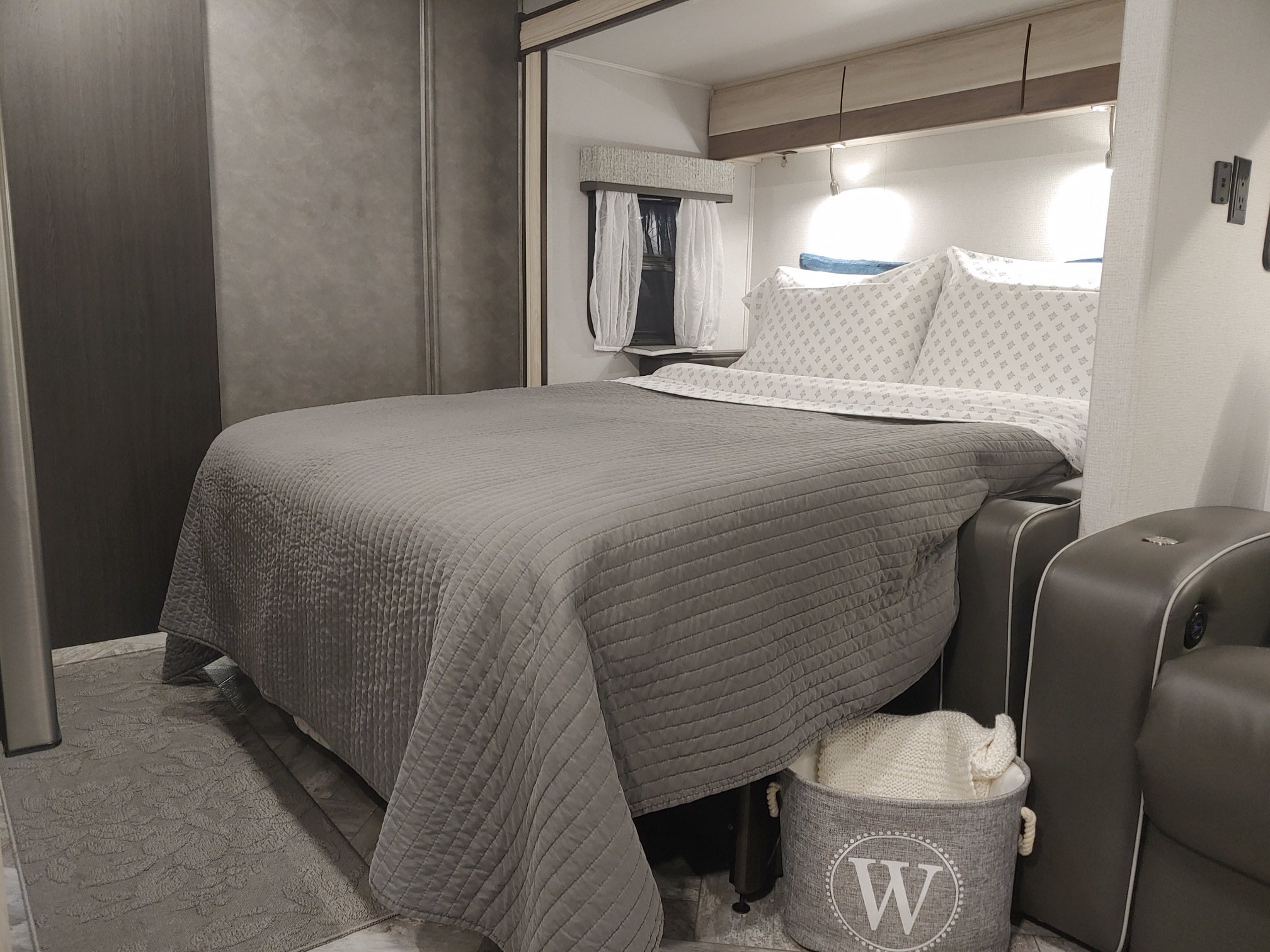 Inside an RV rental: a modern bedroom with a comfortable gray bed, window, and side seating. Enjoy your journey.. Forest River Sunseeker MBS 2022