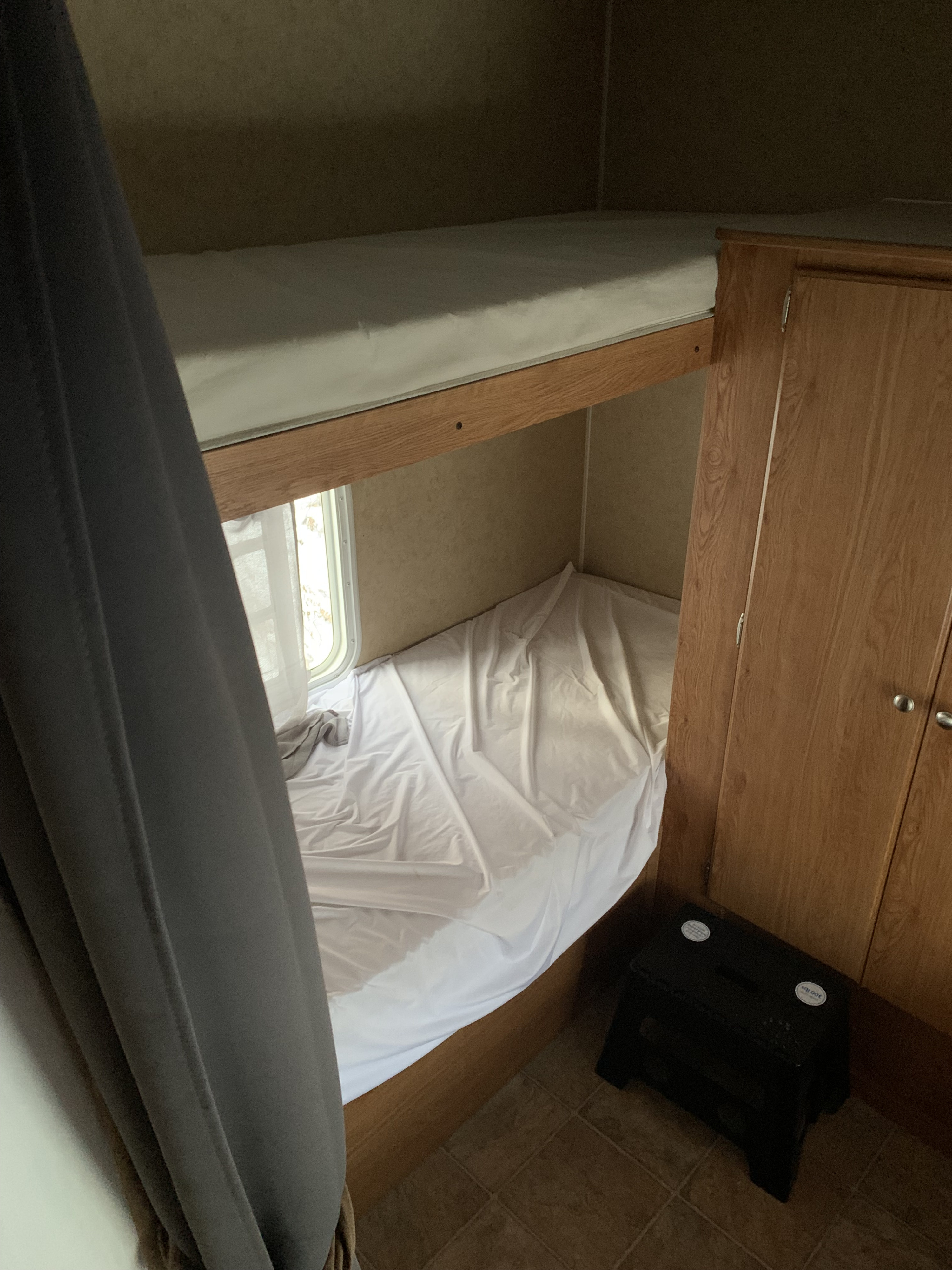 RV rental interior showing bunk beds (white sheets), a window, wooden storage, and a black step stool.. Gulf Stream Kingsport 2007