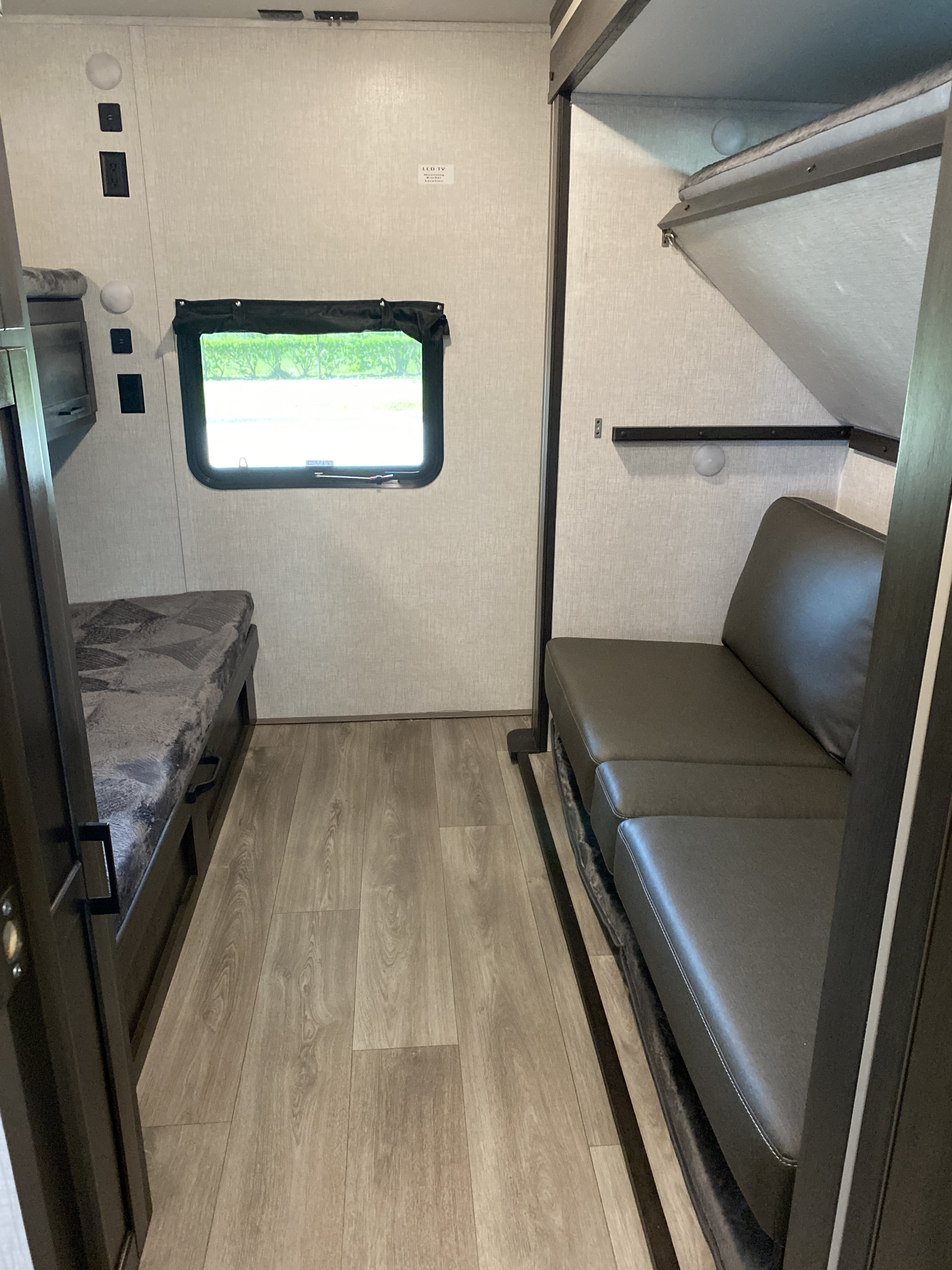 RV rental interior: bunk beds with a window on left, plus a gray convertible sofa with an upper bunk on the right.. Keystone RV Other 2021