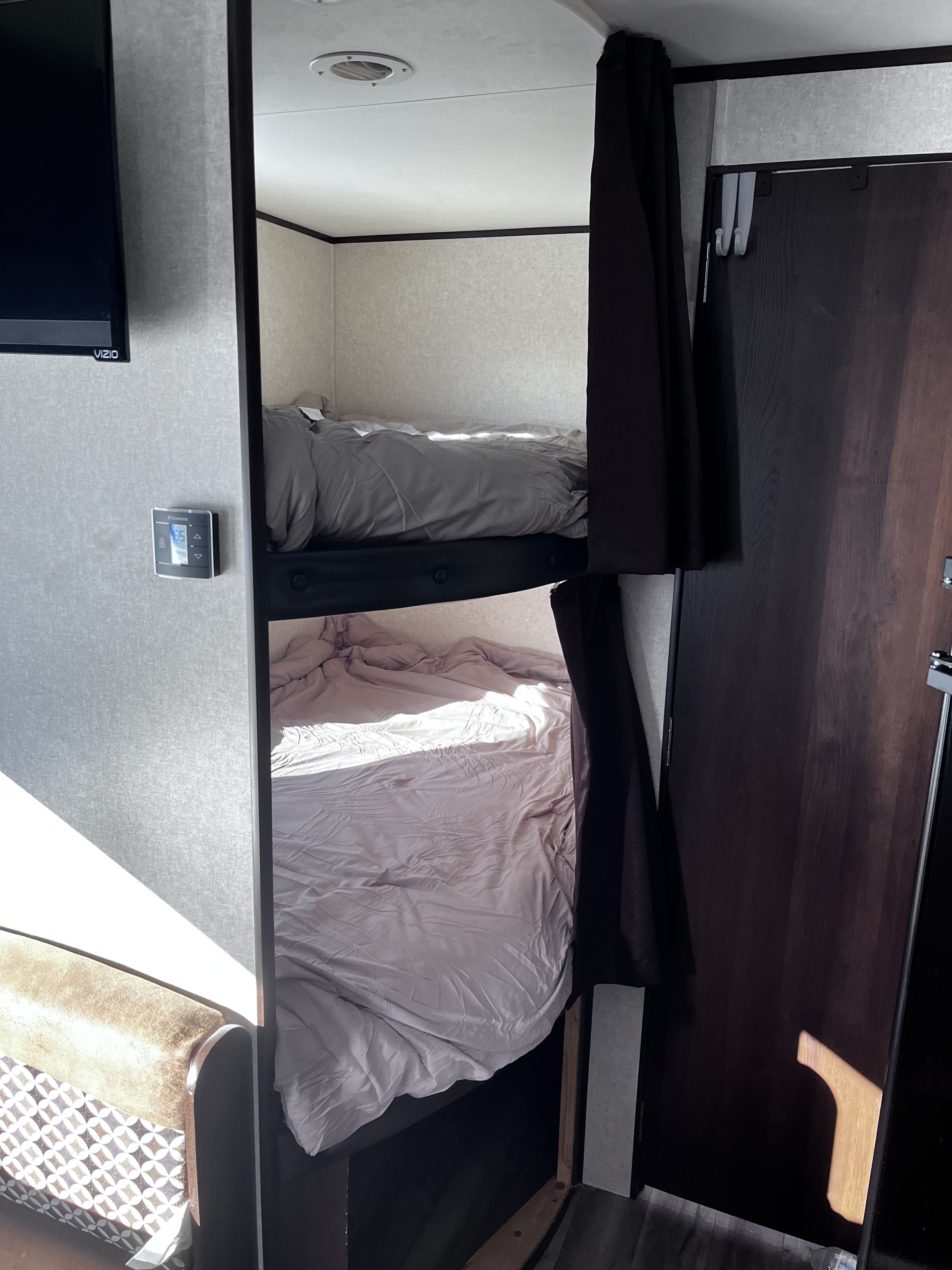 Cozy bunk beds in an RV rental, complete with privacy curtains, a mounted TV, and a Dometic thermostat set to 65.. Jayco Jay Flight SLX 2018