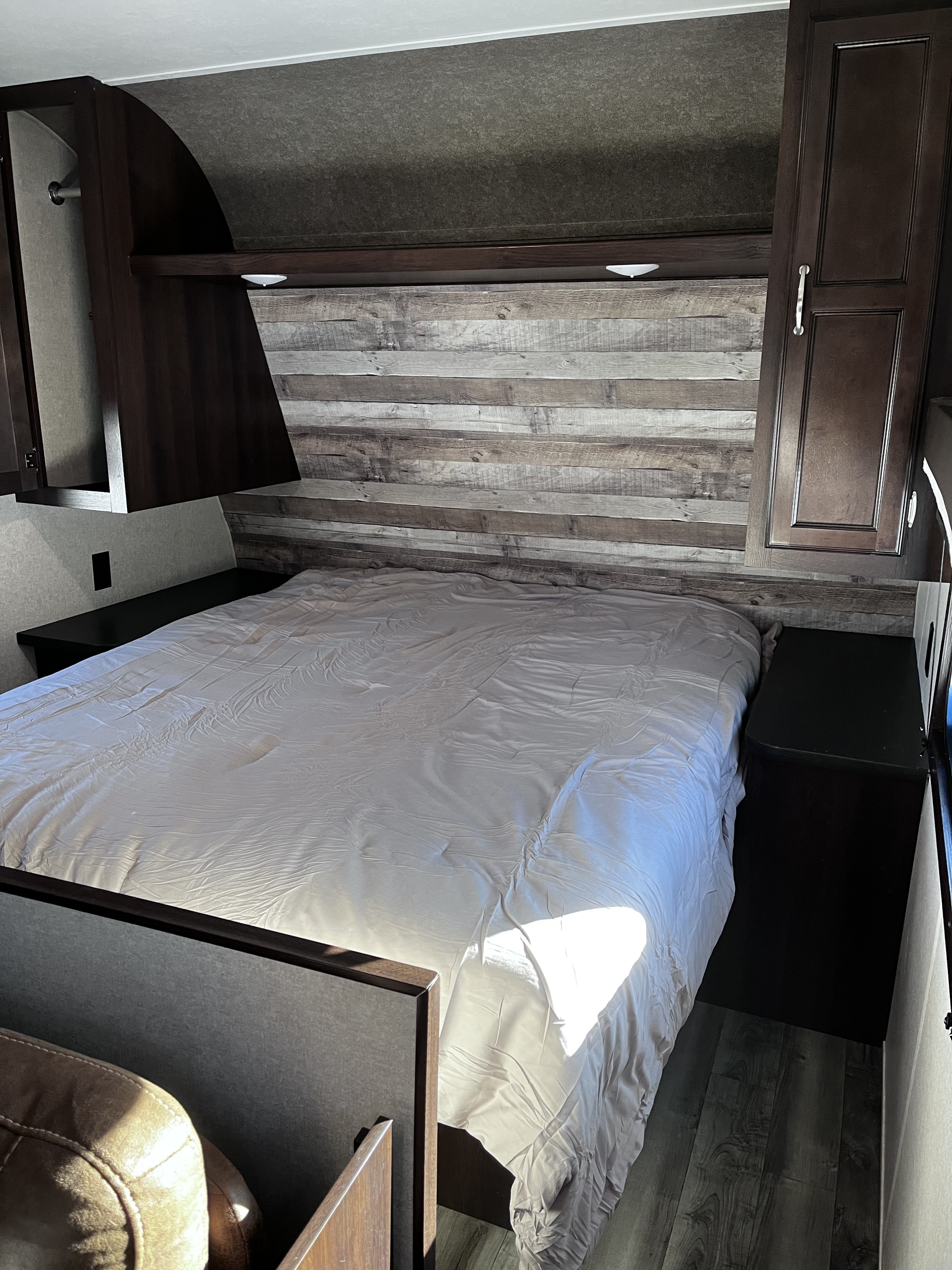 Inside this RV rental: A spacious bedroom featuring a bed with a rustic wood headboard, nightstands, and overhead cabinets.. Jayco Jay Flight SLX 2018