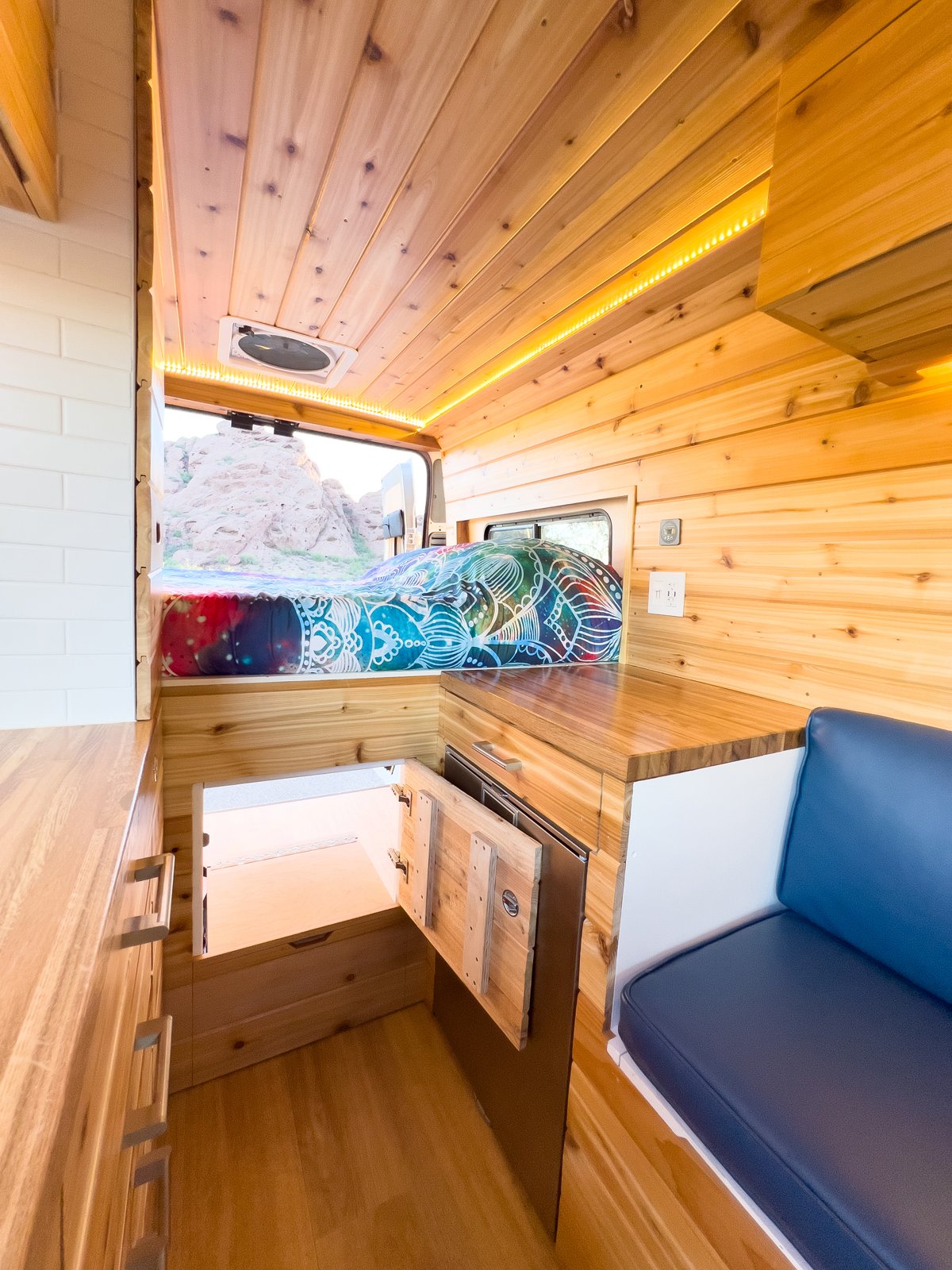 Cozy custom wood RV rental interior with a colorful bed, LED lighting, and ample storage, overlooking a desert view.. Dodge RAM Promaster 2500 High Roof 2021
