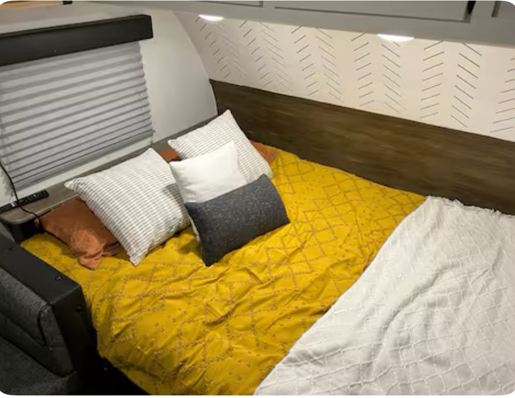 Inviting RV rental bedroom with a comfy yellow bed, accent pillows, and stylish wall decor for a cozy retreat.. Forest River Cherokee Wolf Pup 2022