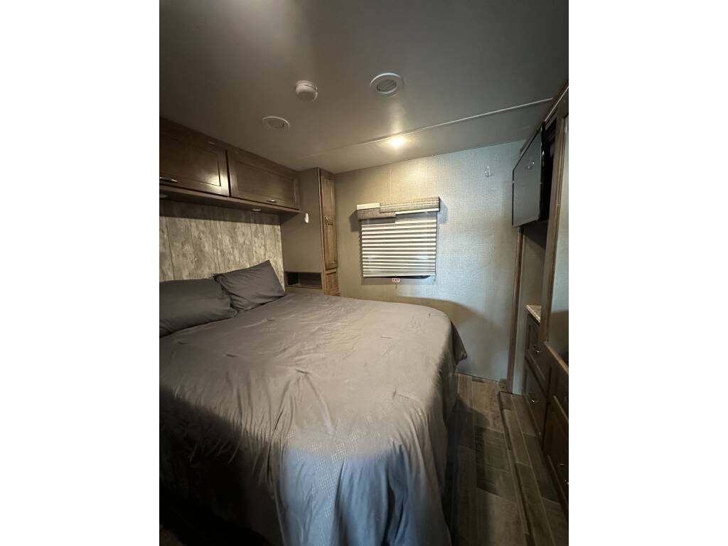 RV rental bedroom: gray queen bed, overhead storage, window, and wall-mounted TV in a compact, modern interior.. Winnebago Intent 2018