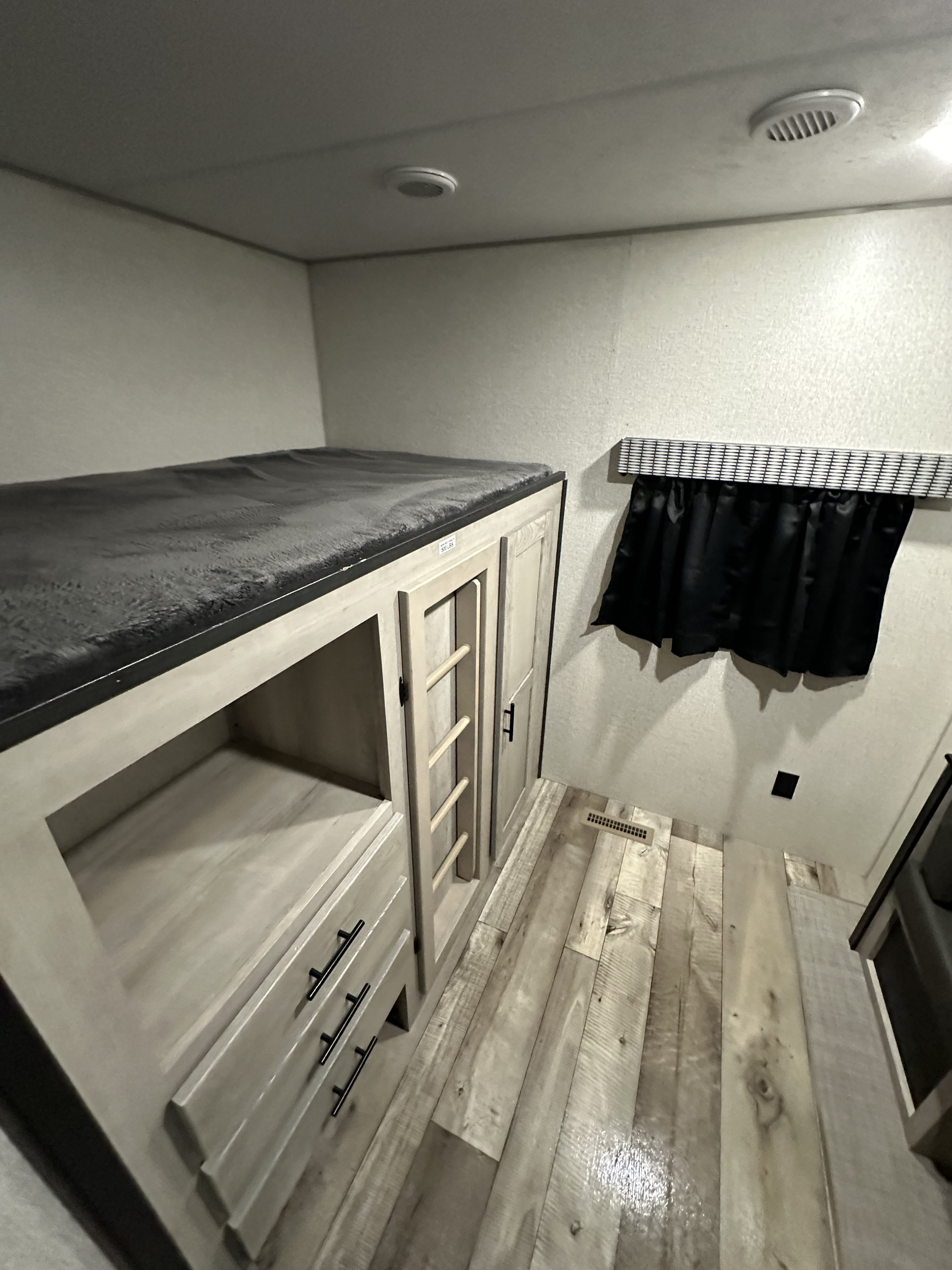 Inside an RV rental: a bunk bed with dark gray bedding above light wood cabinetry with drawers. A ladder and small closet are also visible.. KZ Connect 322BHK 2023