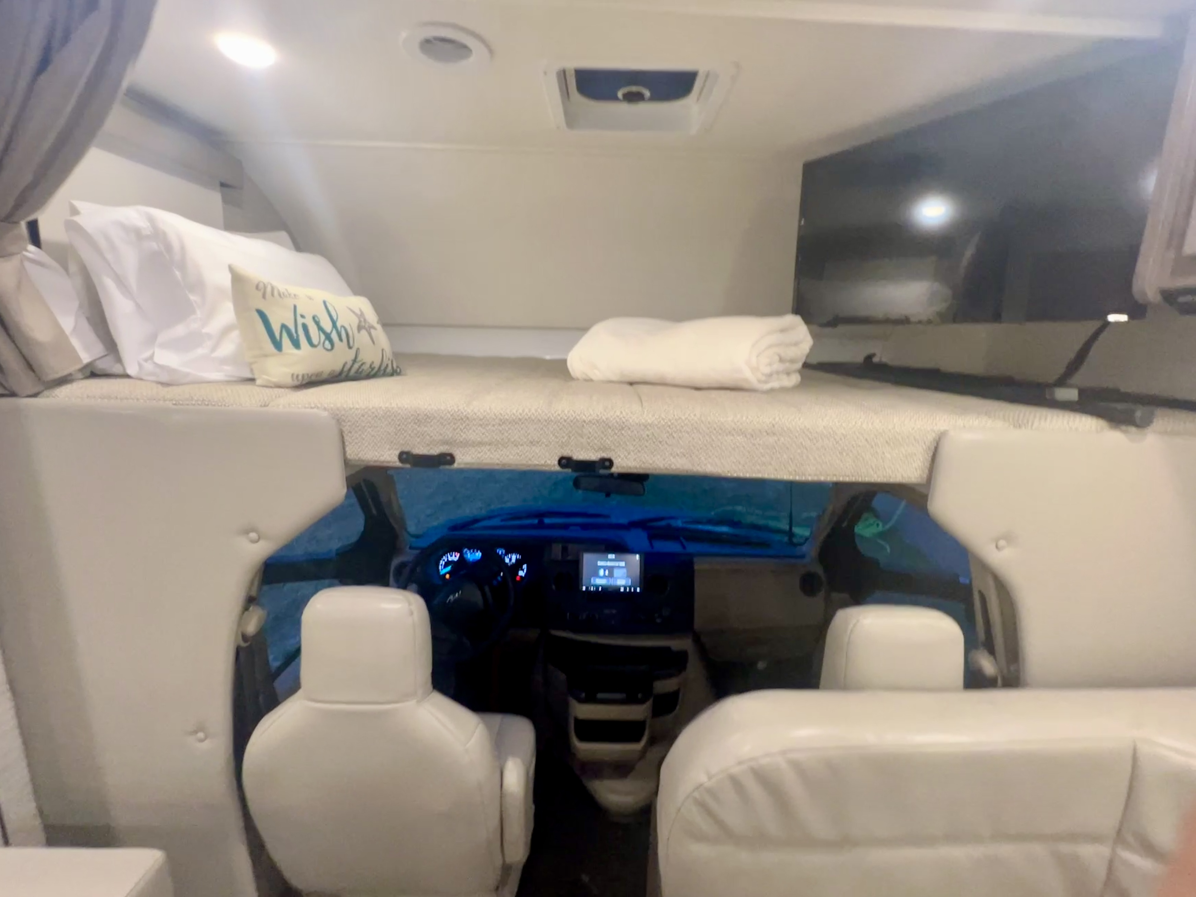 Cozy RV rental interior featuring the comfortable overhead bunk with bedding and the spacious front cockpit area.. Winnebago Spirit 2025