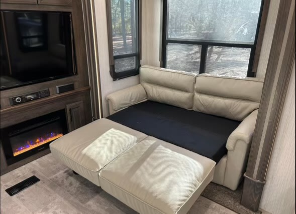 RV rental interior showing a cream sleeper sofa pulled out into a bed, with a TV and electric fireplace.. Heartland RVs Landmark 365 2021