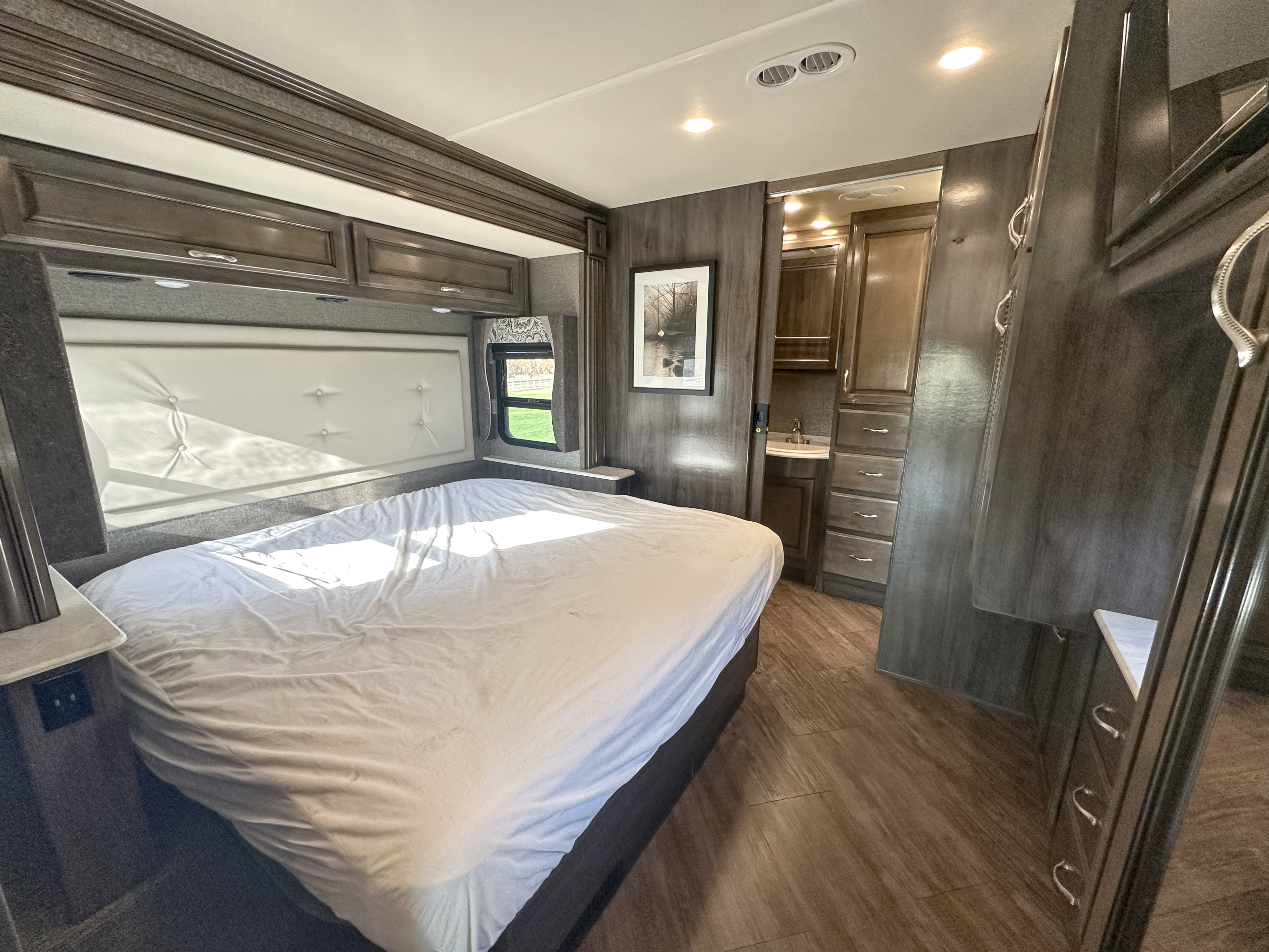 Comfortable RV rental bedroom with white bed, overhead cabinets, and a compact bathroom.. Fleetwood Bounder 2018