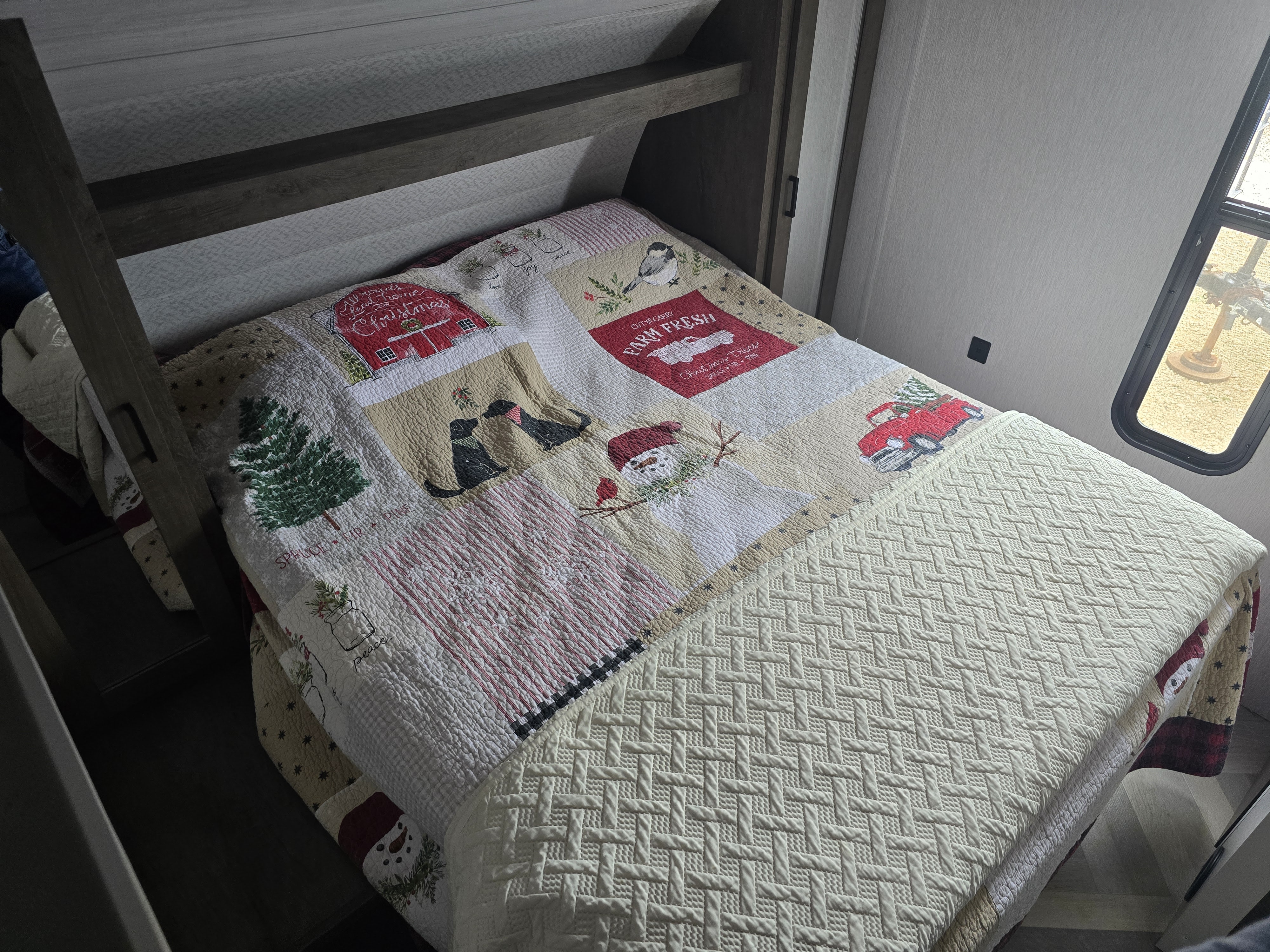 This cozy rv rental bedroom features a Christmas quilt, illustrating a compact and festive sleeping area.. Forest River Wildwood X-Lite 2022