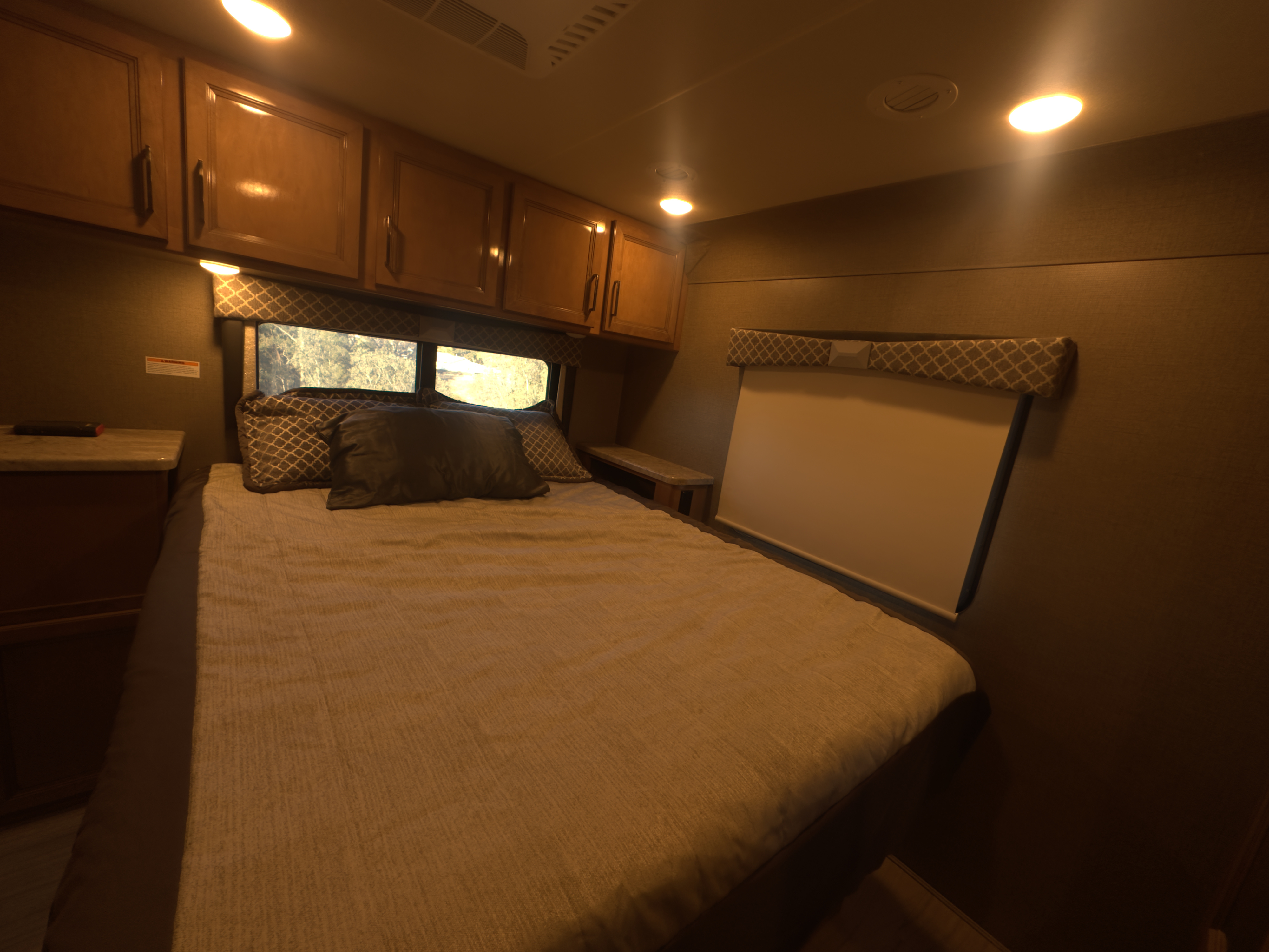 Comfortable RV rental bedroom: cozy bed, nightstand, windows, overhead cabinets, and warm lighting.. Thor Quantum 2021
