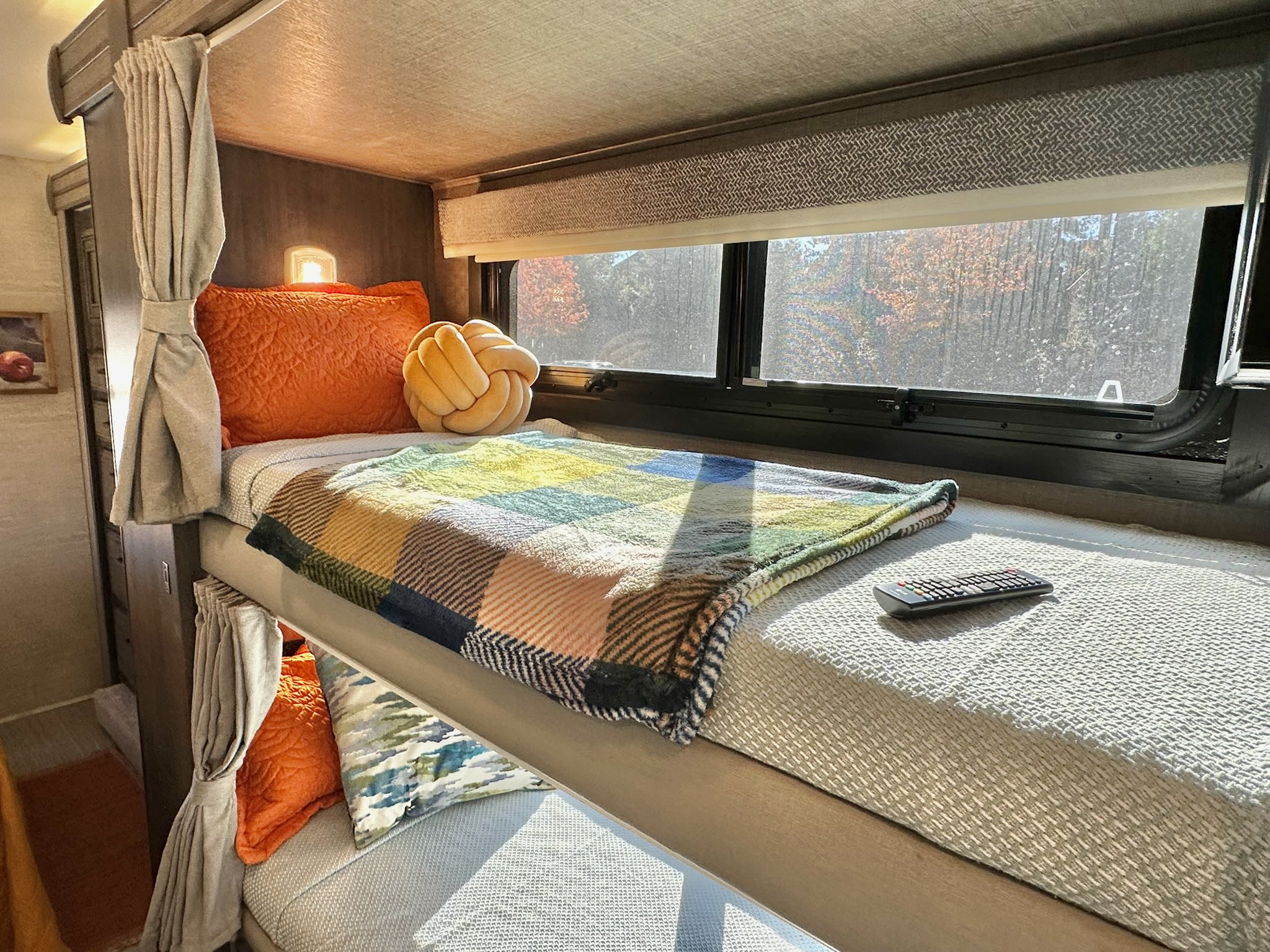 An RV rental's cozy bunk beds, complete with colorful blankets, pillows, and a scenic window view.. Entegra Coach Esteem 2023