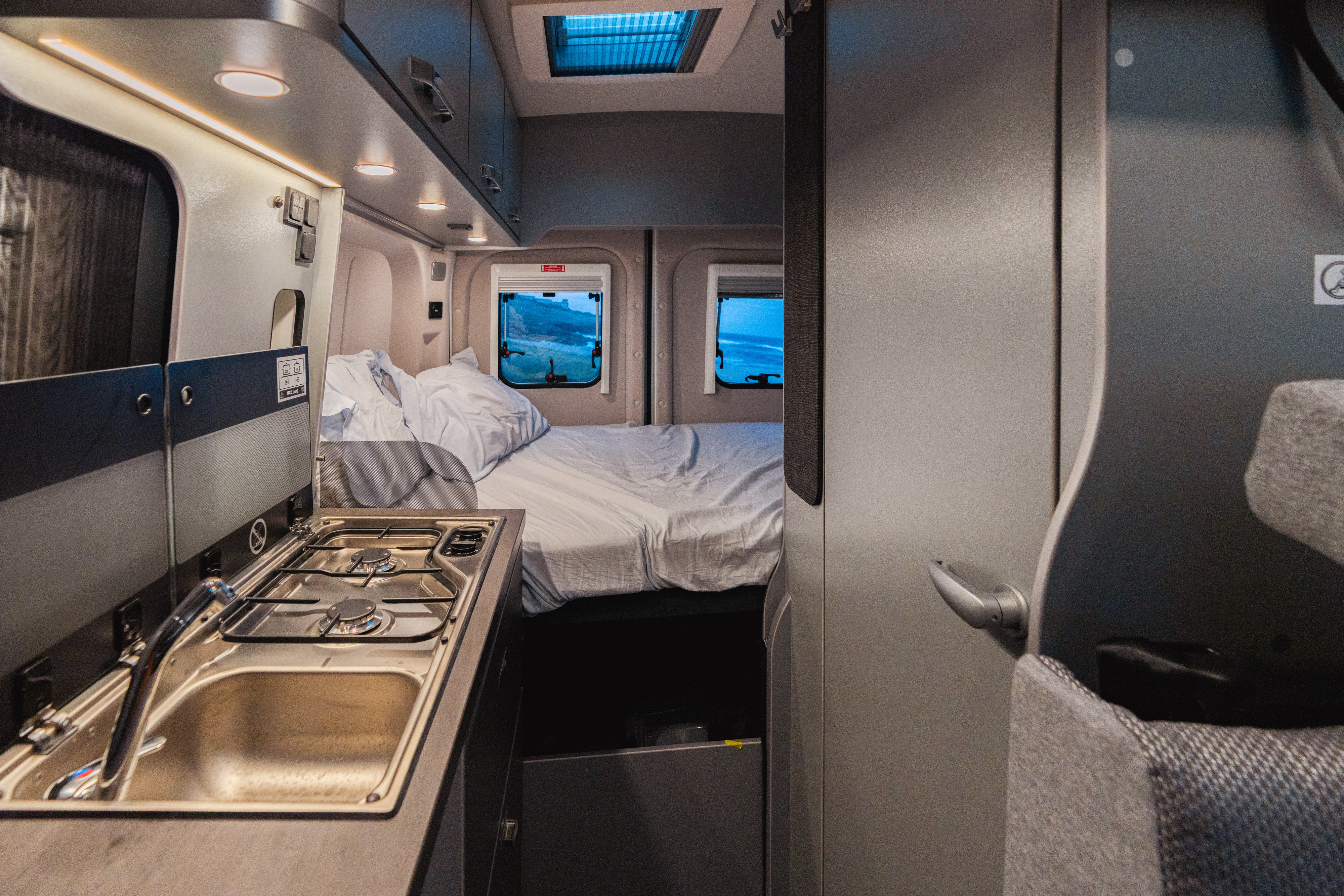 Explore this RV rental's compact interior, featuring a built-in kitchen, sink, stove, and bed with ocean views.. weinsberg 550 2024