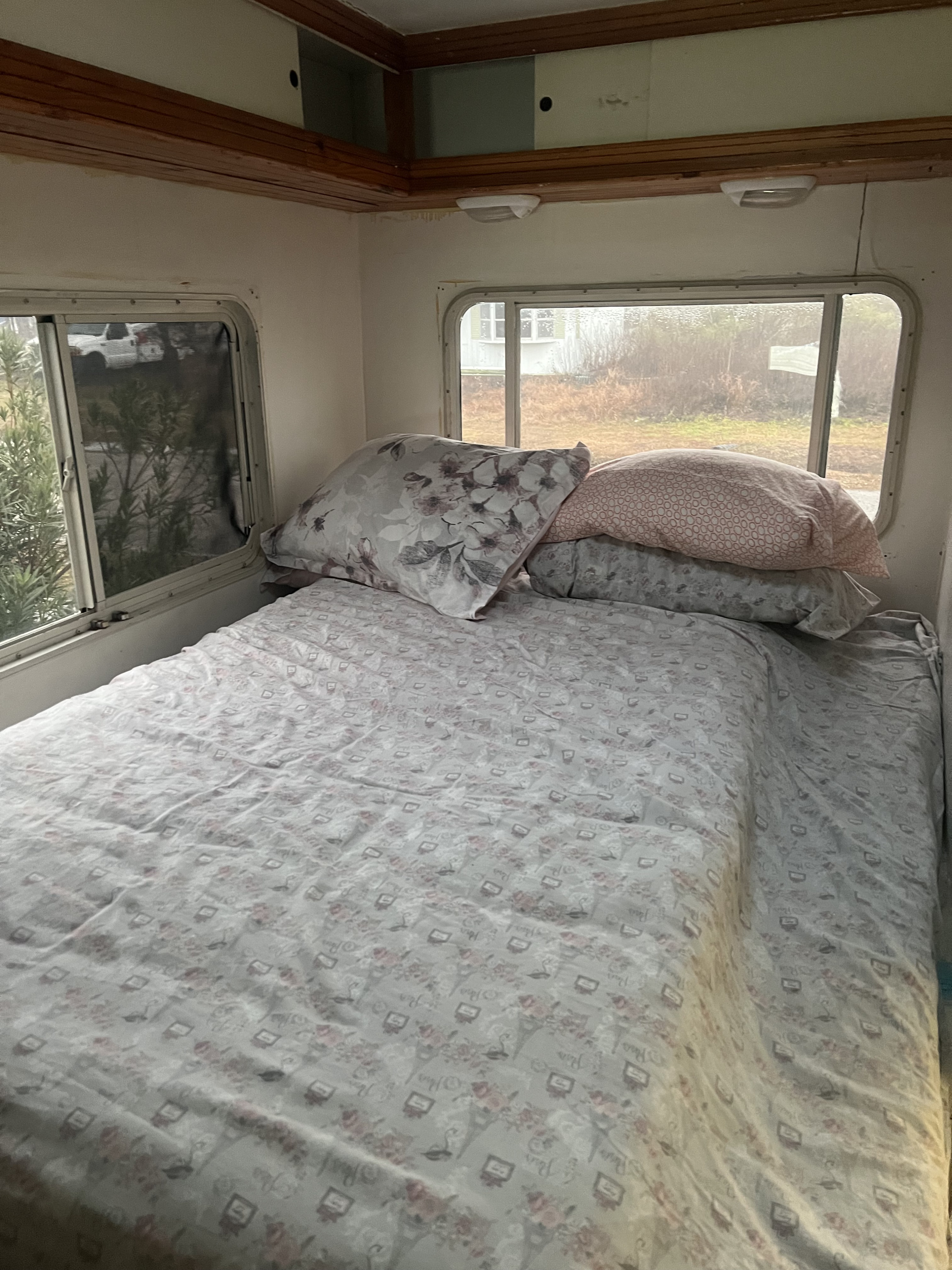 Cozy RV rental bedroom with a patterned bed, pillows, and large windows revealing outdoor scenery.. Coachmen Freelander 2008