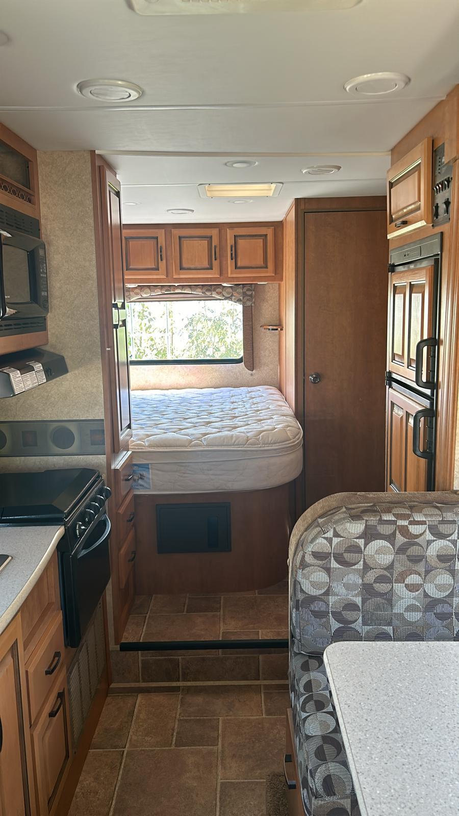 Inside this RV rental: kitchen with stove/microwave, a cozy bed nook, and dining area with a patterned bench.. Forester Forester Motorhome 2011