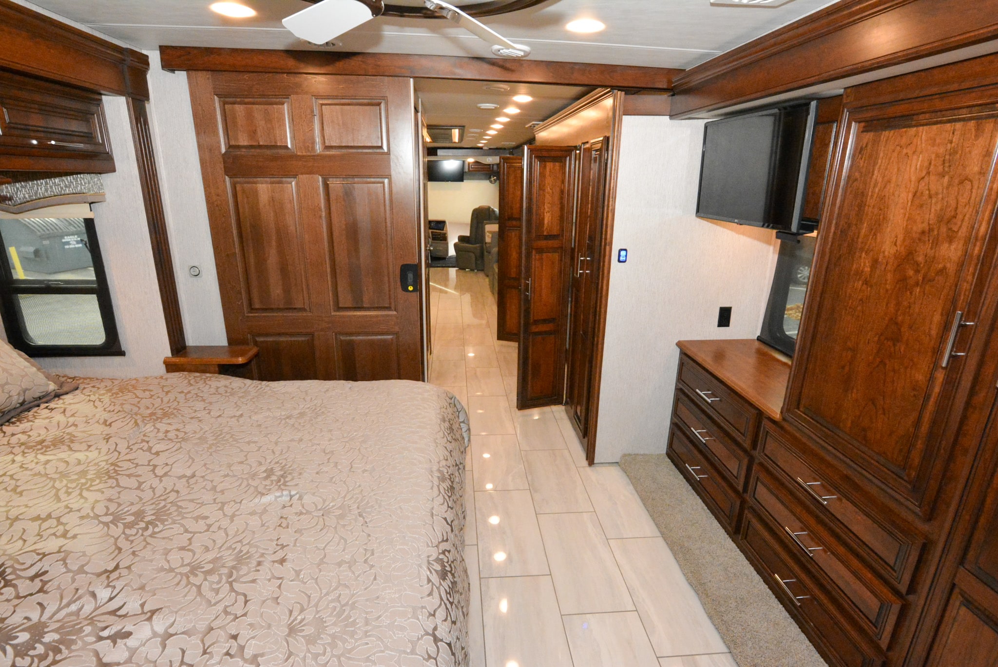Inside an RV rental: a plush bedroom, rich wood cabinets & doors, and a tiled hall leading to the living area. Perfect for travel.. Forest River Berkshire 2021
