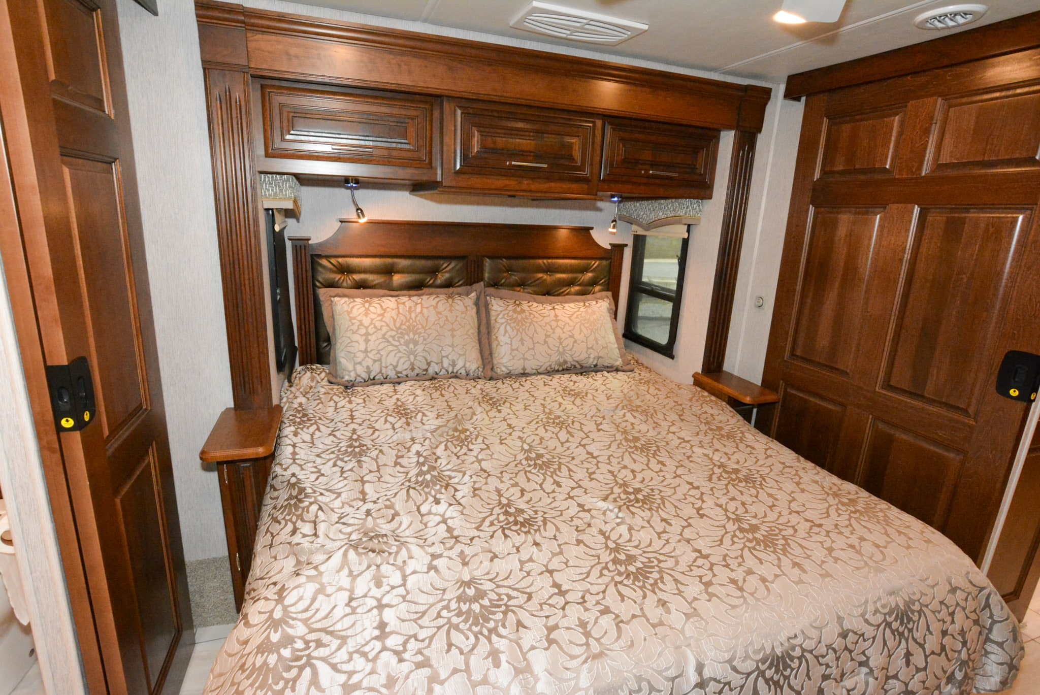 Plush RV rental bedroom features a queen bed, dark wood cabinetry, side tables, and ample lighting for cozy nights.. Forest River Berkshire 2021