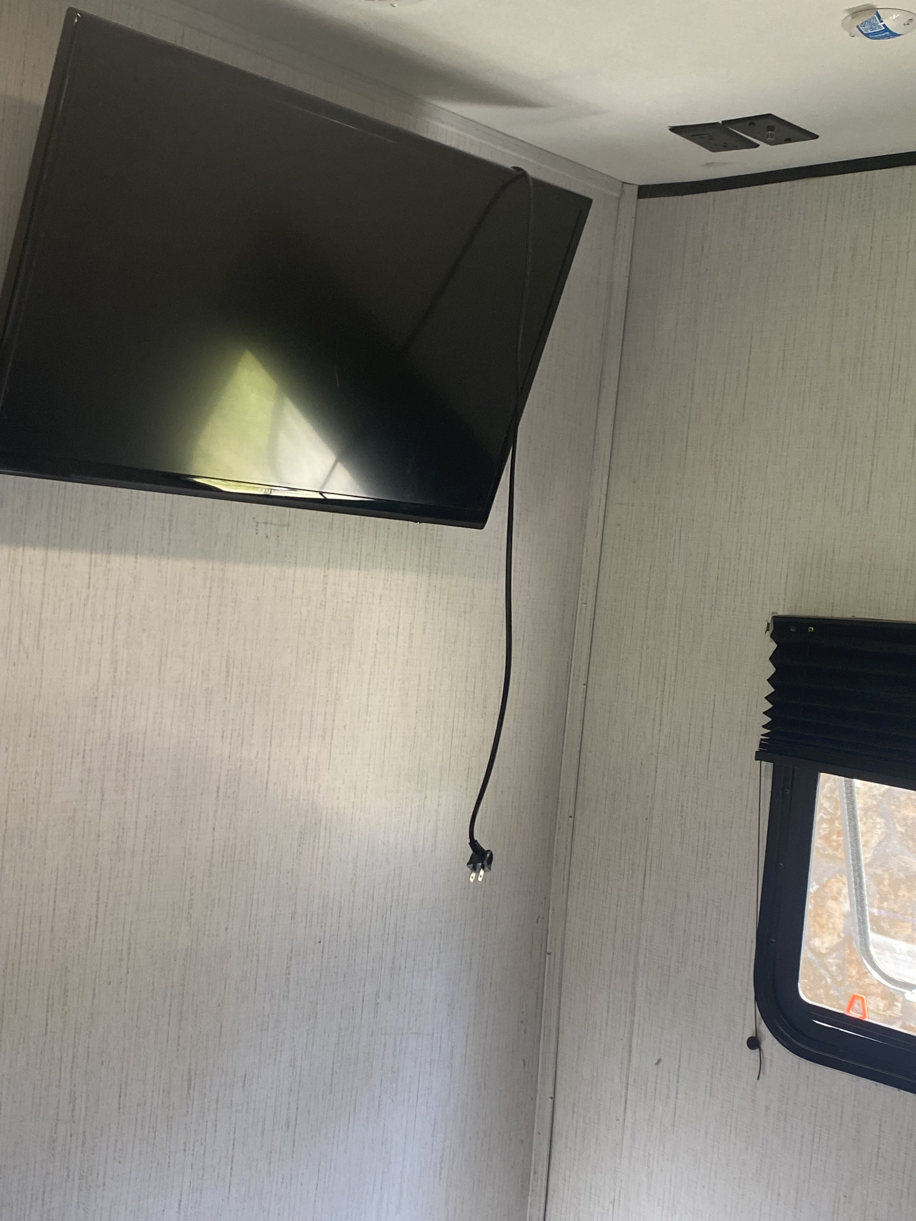 RV rental: TV mounted in a compact interior, with power cord hanging freely. Window blinds on light textured walls.. Heartland RVs Prowler 2021