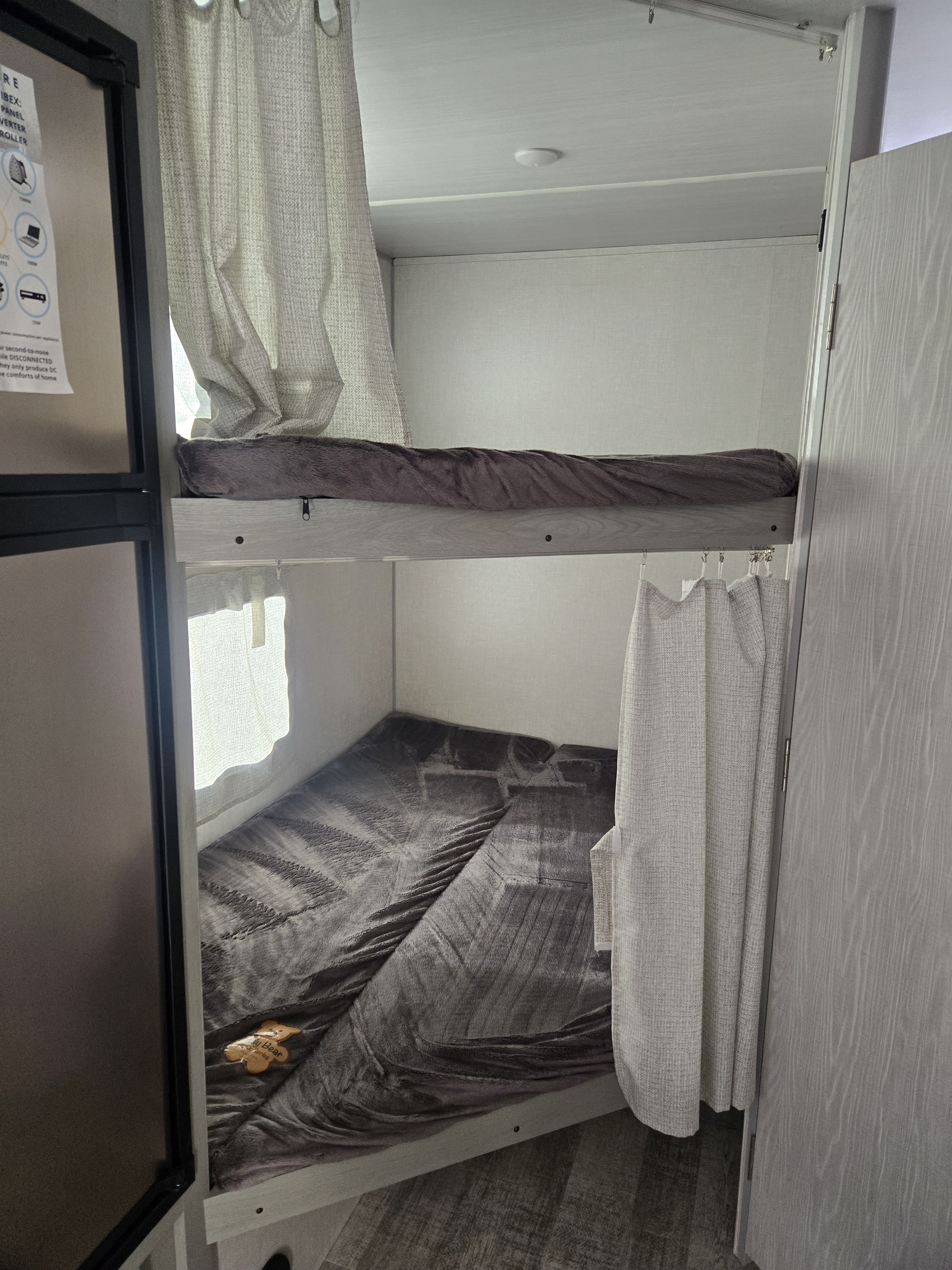 RV rental interior featuring cozy bunk beds with privacy curtains and soft gray bedding, ideal for family travel.. Forest River Ibex 2023