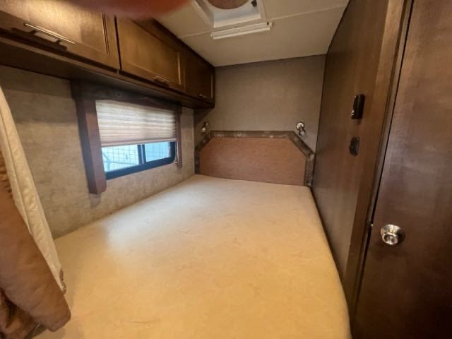 View inside an RV rental bedroom with a light-colored mattress, overhead wood cabinets, and a window.. Adventurer Adventurer Motorhome 2017