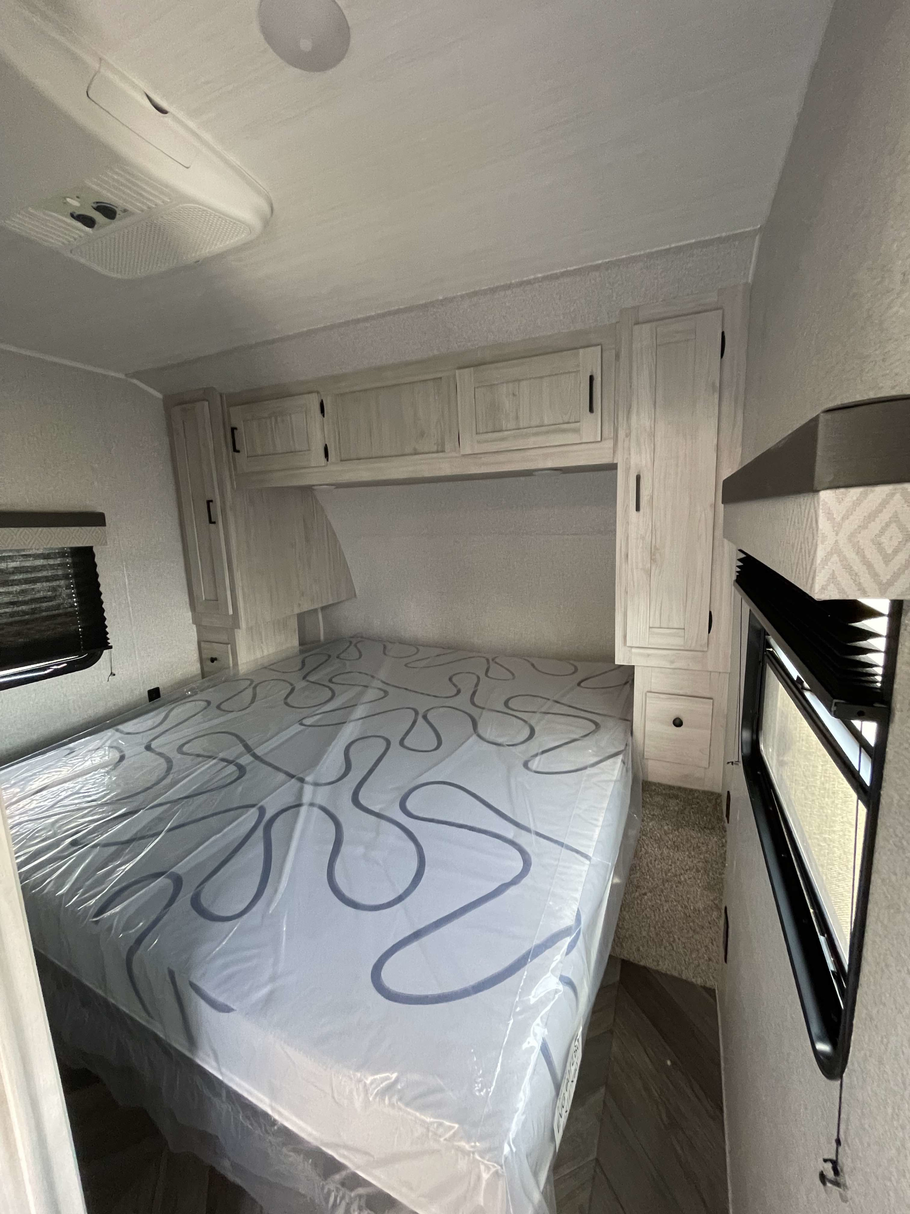 RV rental bedroom showcasing a plastic-covered mattress, light wood cabinets, and a ceiling AC unit for guest comfort.. East to West Della Terra 2022