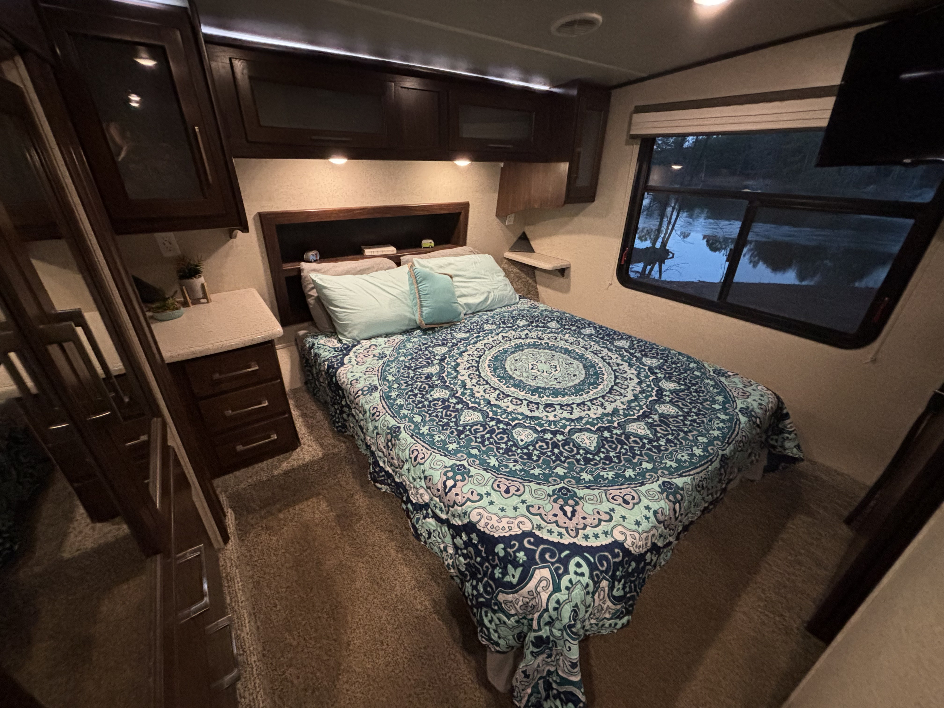 Cozy RV rental bedroom with a comfy bed, overhead cabinets, and a serene water view from the window.. Heartland Cyclone 2018