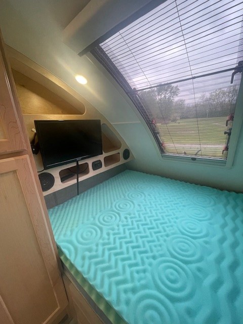 Cozy RV rental interior: teal foam bed, TV, and large window with blinds overlooking nature. Compact and comfortable.. Xtreme Outdoors TearDrop 2022