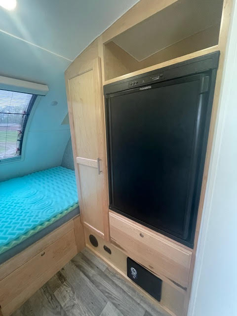 Compact RV rental interior with a cozy bed, built-in Dometic fridge, and light wood cabinetry.. Xtreme Outdoors TearDrop 2022