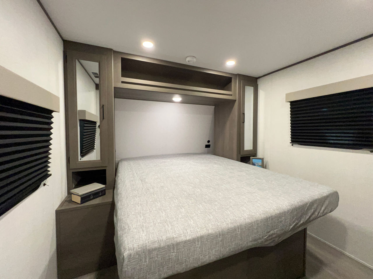 RV rental bedroom featuring a large bed, built-in cabinetry, and drawn privacy blinds on side windows, perfect for travel.. Grand Design Transcend model TR22RBX-2025 2025