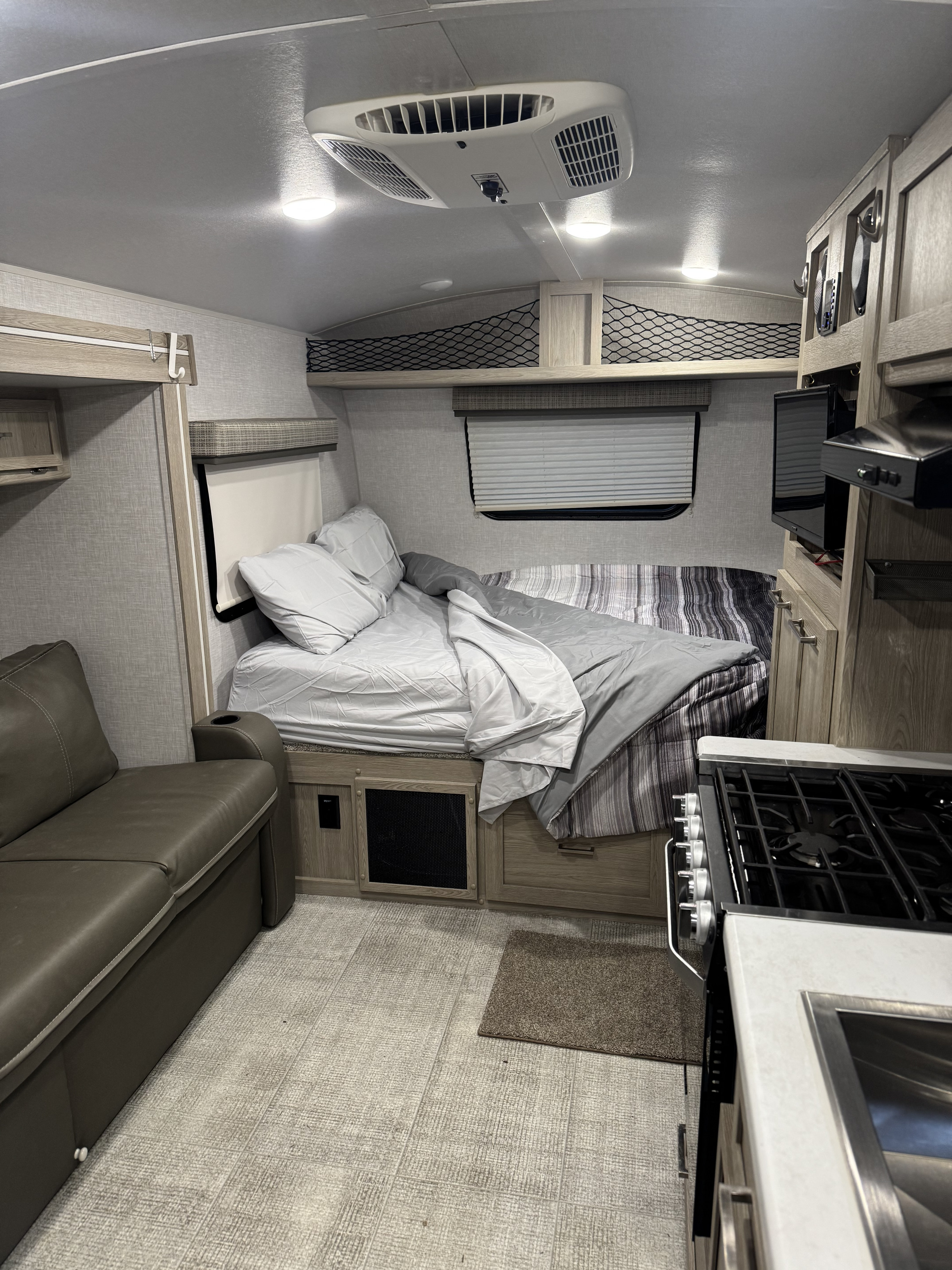 Inside an rv rental: a cozy bedroom with light gray bedding, a brown leather sofa, and a compact kitchen.. Forest River Flagstaff E-Pro 2021