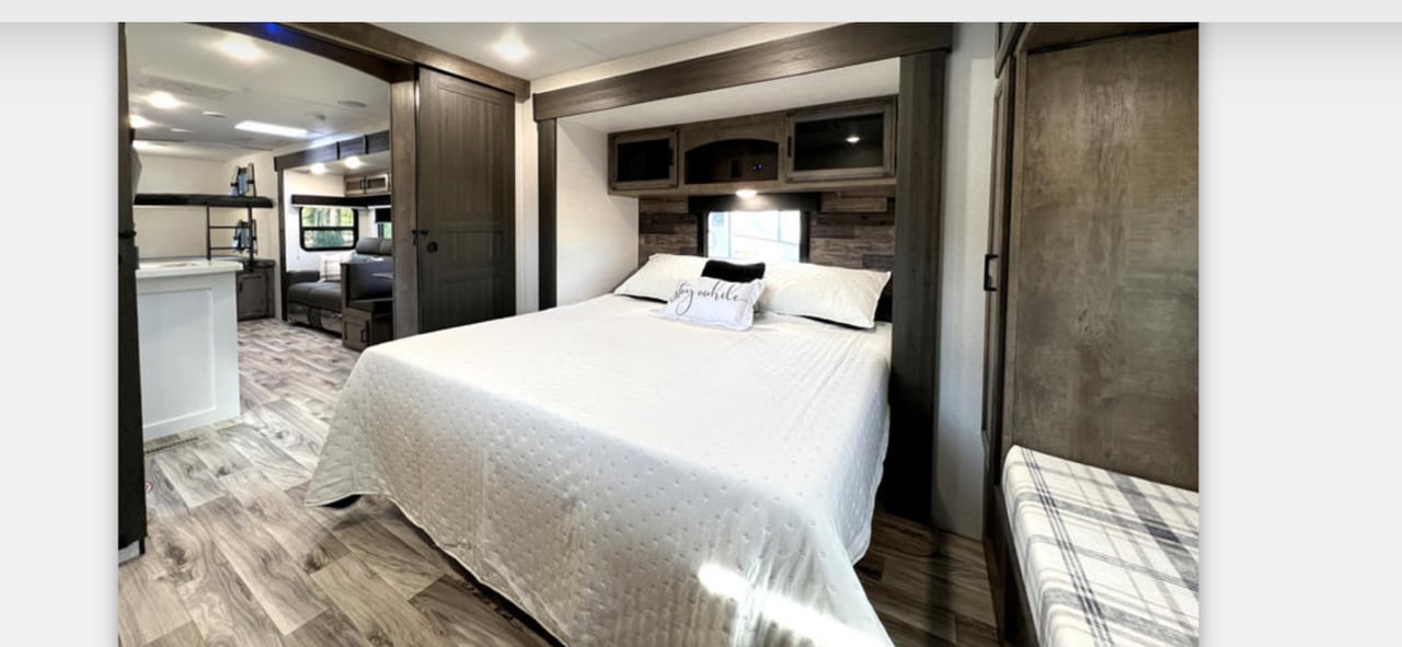 Modern RV rental interior showing a spacious bedroom with a queen bed and a view of the living area with bunk beds.. Sport Trek Touring Edition 2023
