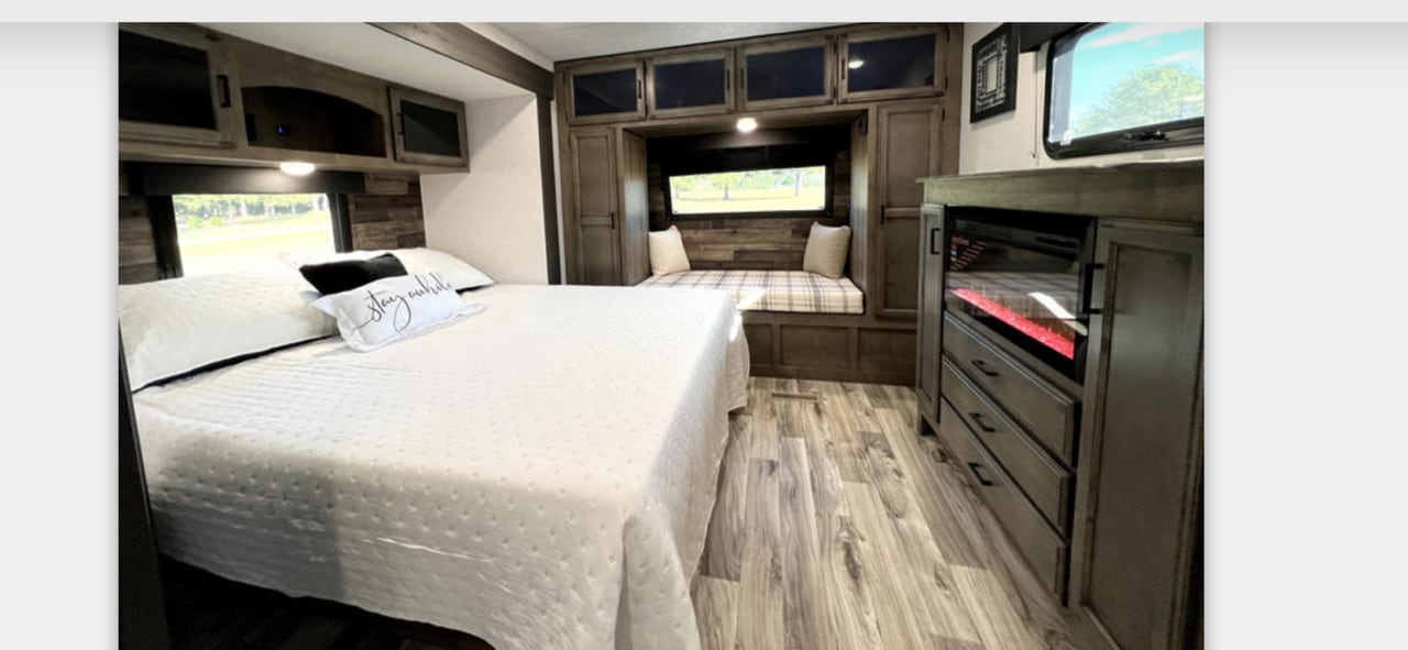 Spacious RV rental bedroom with a comfortable bed, built-in window seat, and electric fireplace, offering a cozy retreat.. Sport Trek Touring Edition 2023