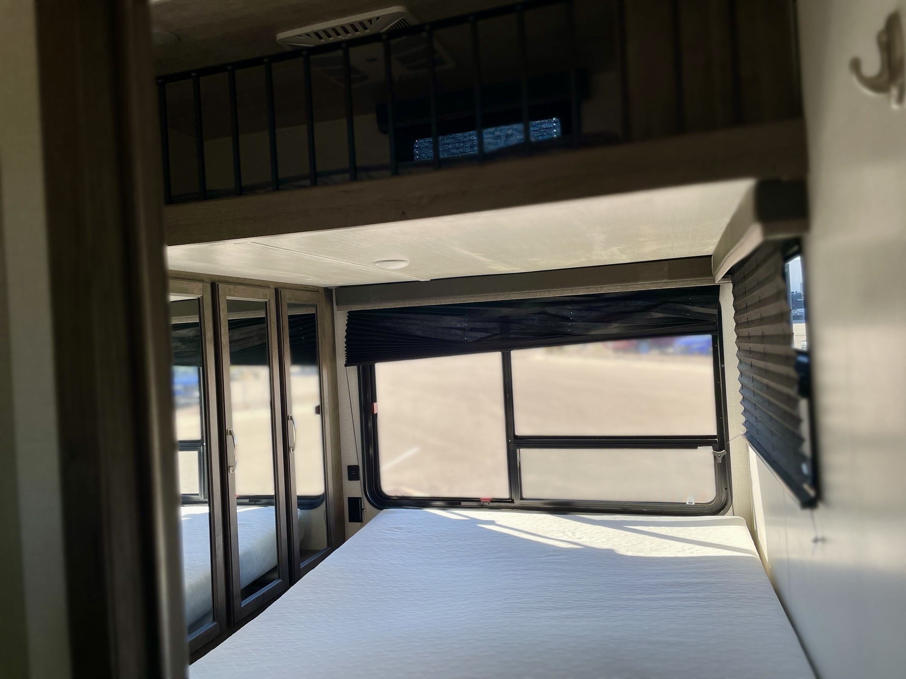 Inside an RV rental: a bright bedroom with a bed, large windows, mirrored closets, and a loft overhead. Ideal for your next adventure.. Keystone Cougar 2021