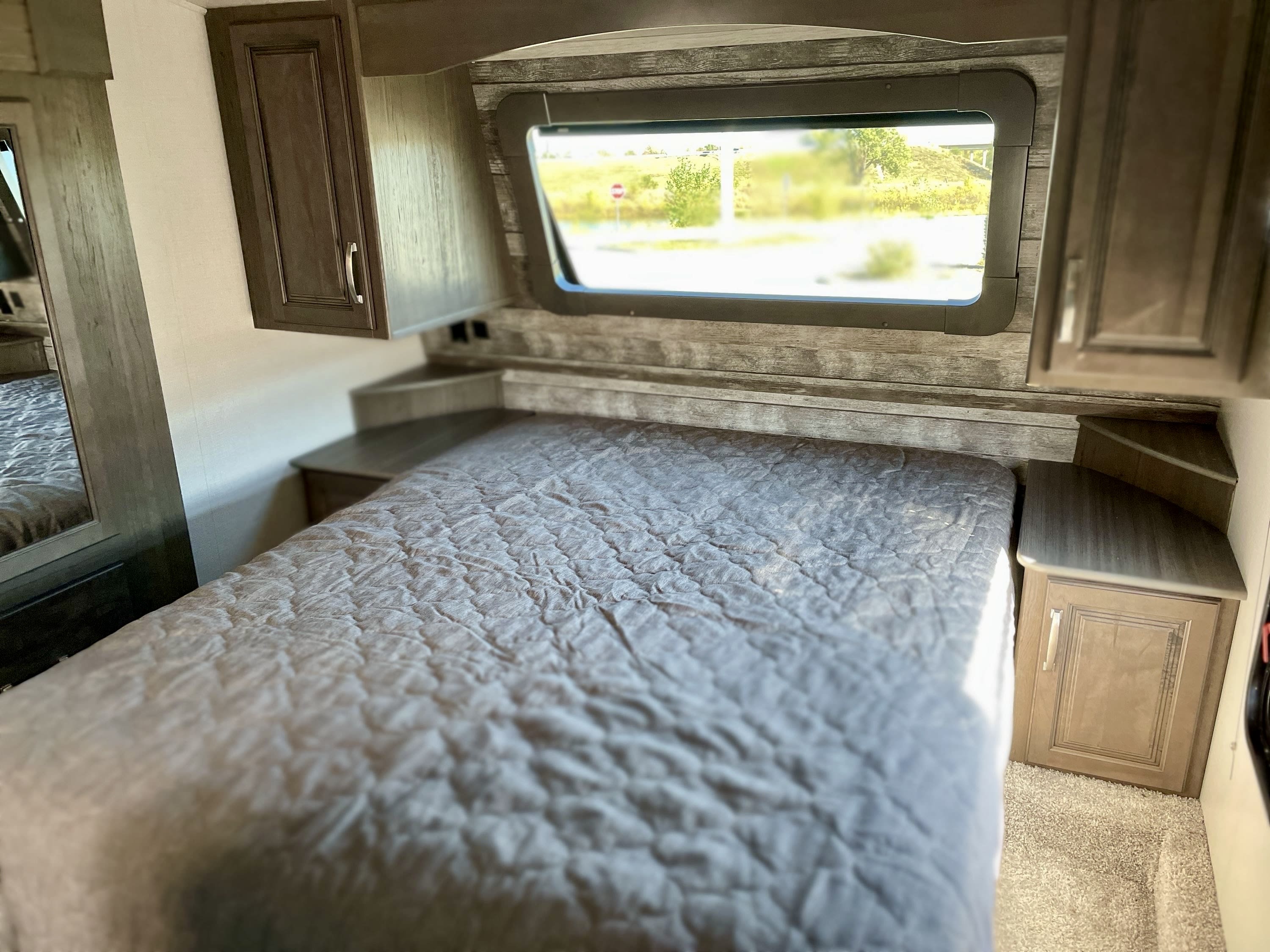 Cozy RV rental bedroom featuring a comfortable bed, window with outdoor view, and convenient storage solutions.. Keystone Cougar 2021