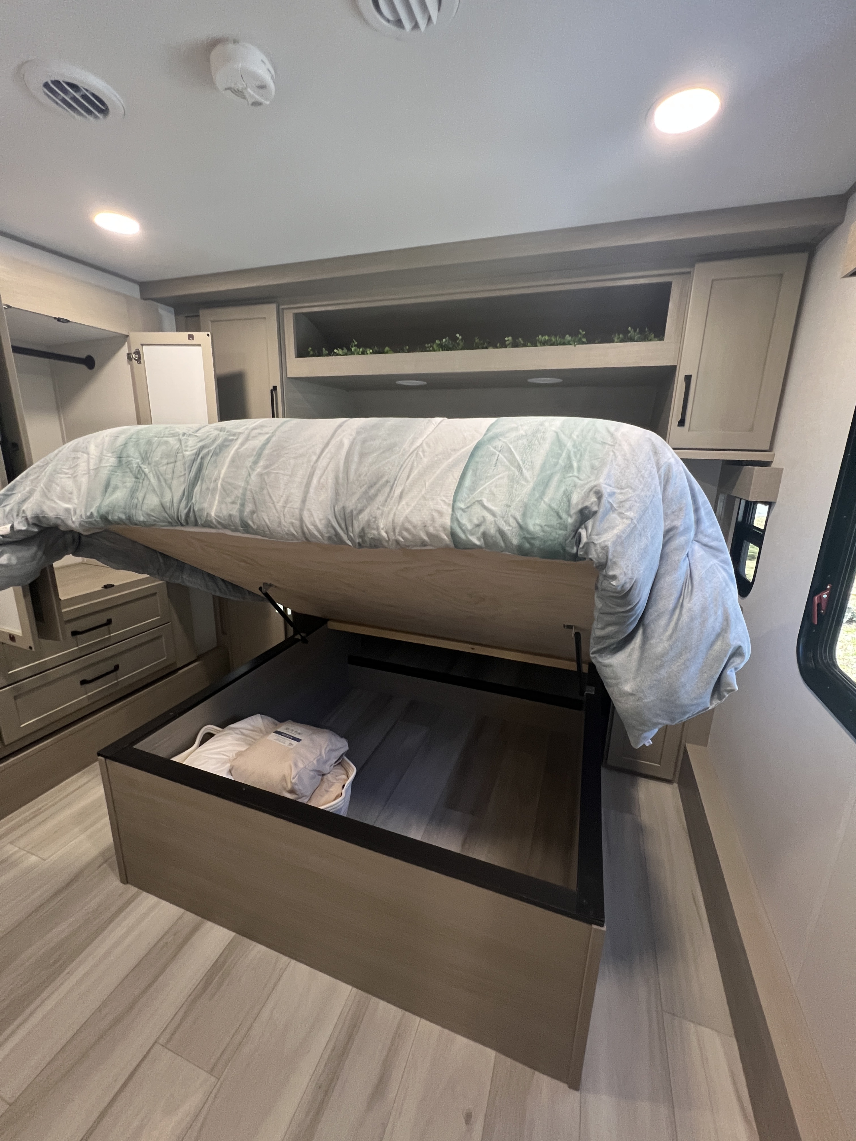 Efficient RV rental bedroom featuring a lifting bed for large storage, overhead cabinets, and a side closet.. Grand Design Momentum 2025