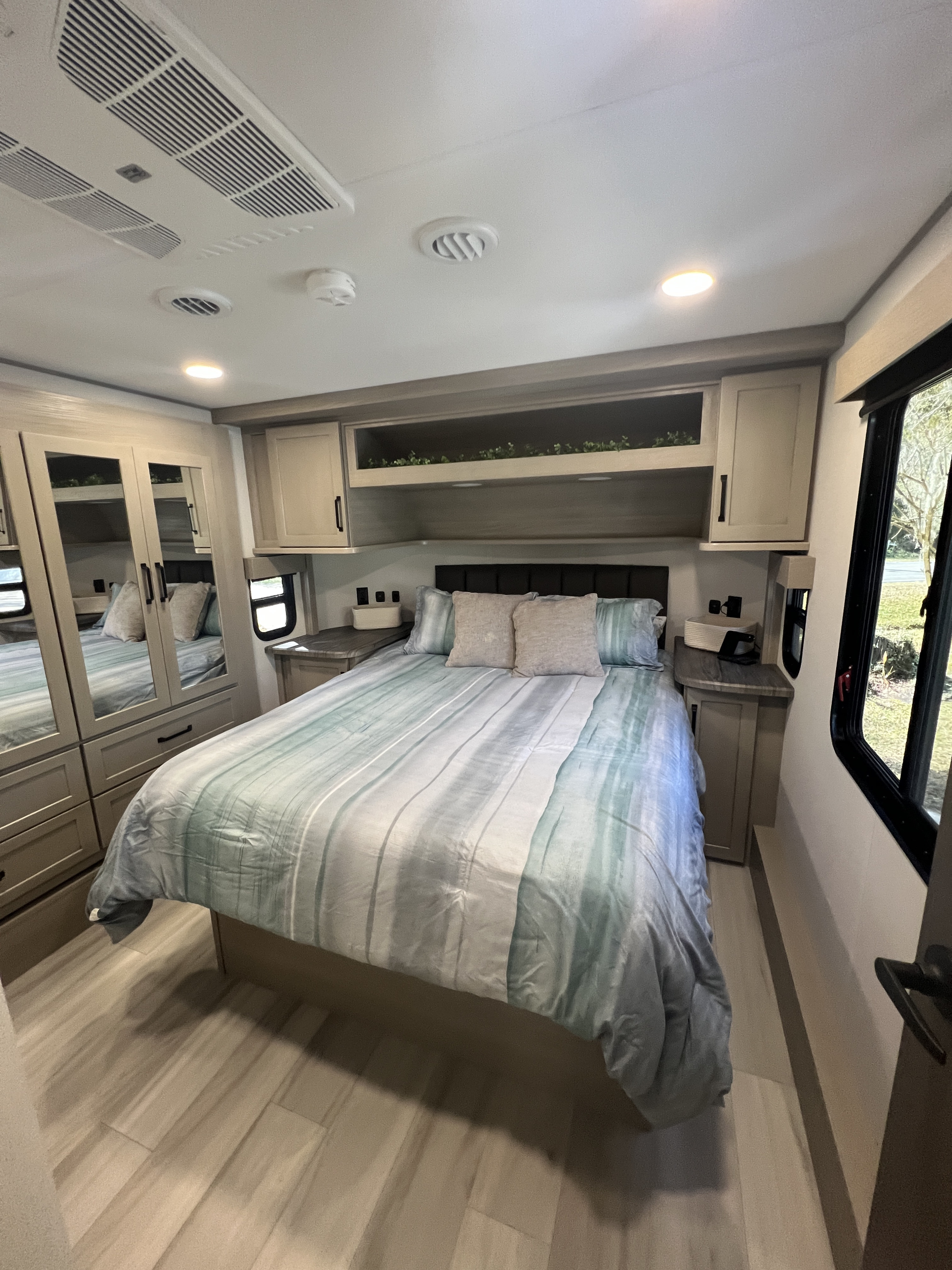 Well-appointed RV rental bedroom features a queen bed, mirrored closet, and ample overhead storage.. Grand Design Momentum 2025