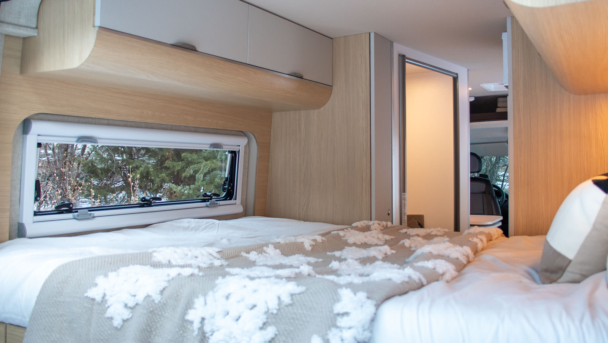 Cozy RV rental bedroom with window view, soft bedding, and overhead storage, perfect for a comfortable travel experience.. Noovo Lite 2025
