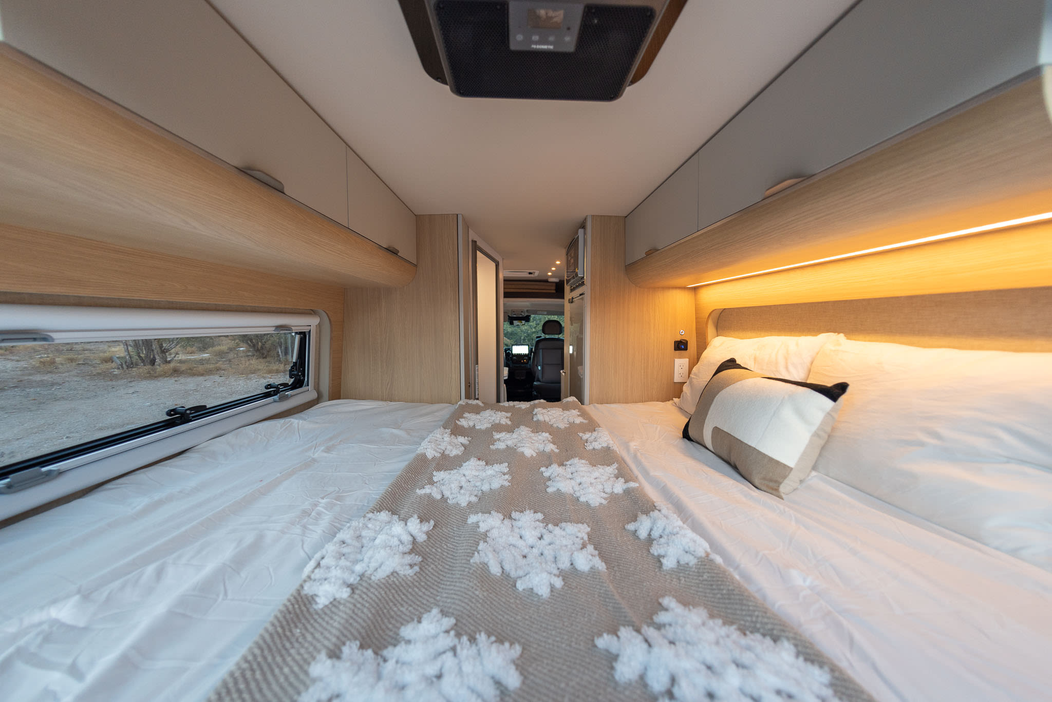 Clean, spacious RV rental interior with comfortable bed, warm lighting, and integrated storage, looking towards the cockpit.. Noovo Lite 2025