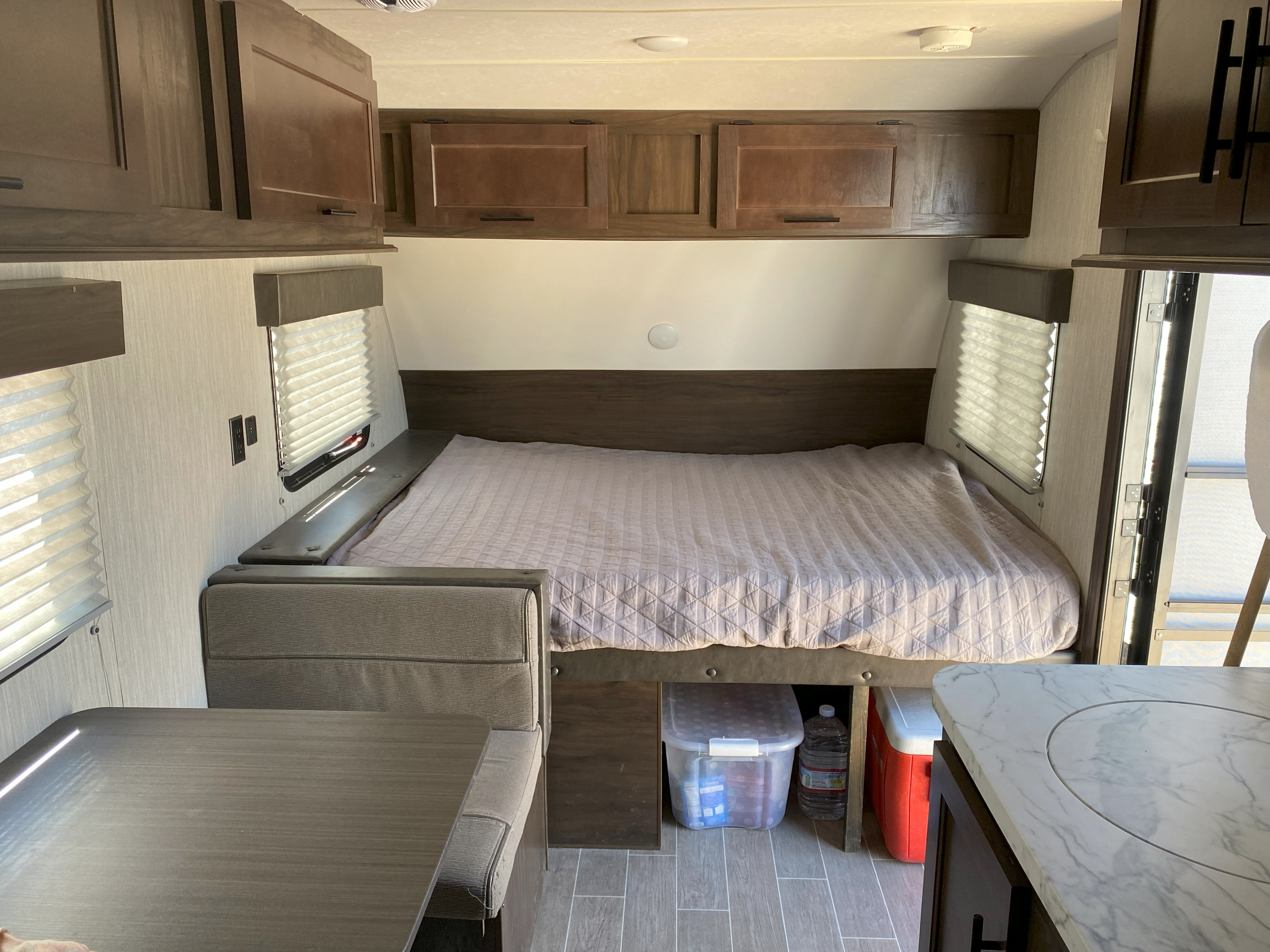 View of an RV rental interior: bed with quilted blanket, dinette, wood cabinets, and marble-look counter. Storage visible.. Forest River Cherokee Wolf Pup 2020