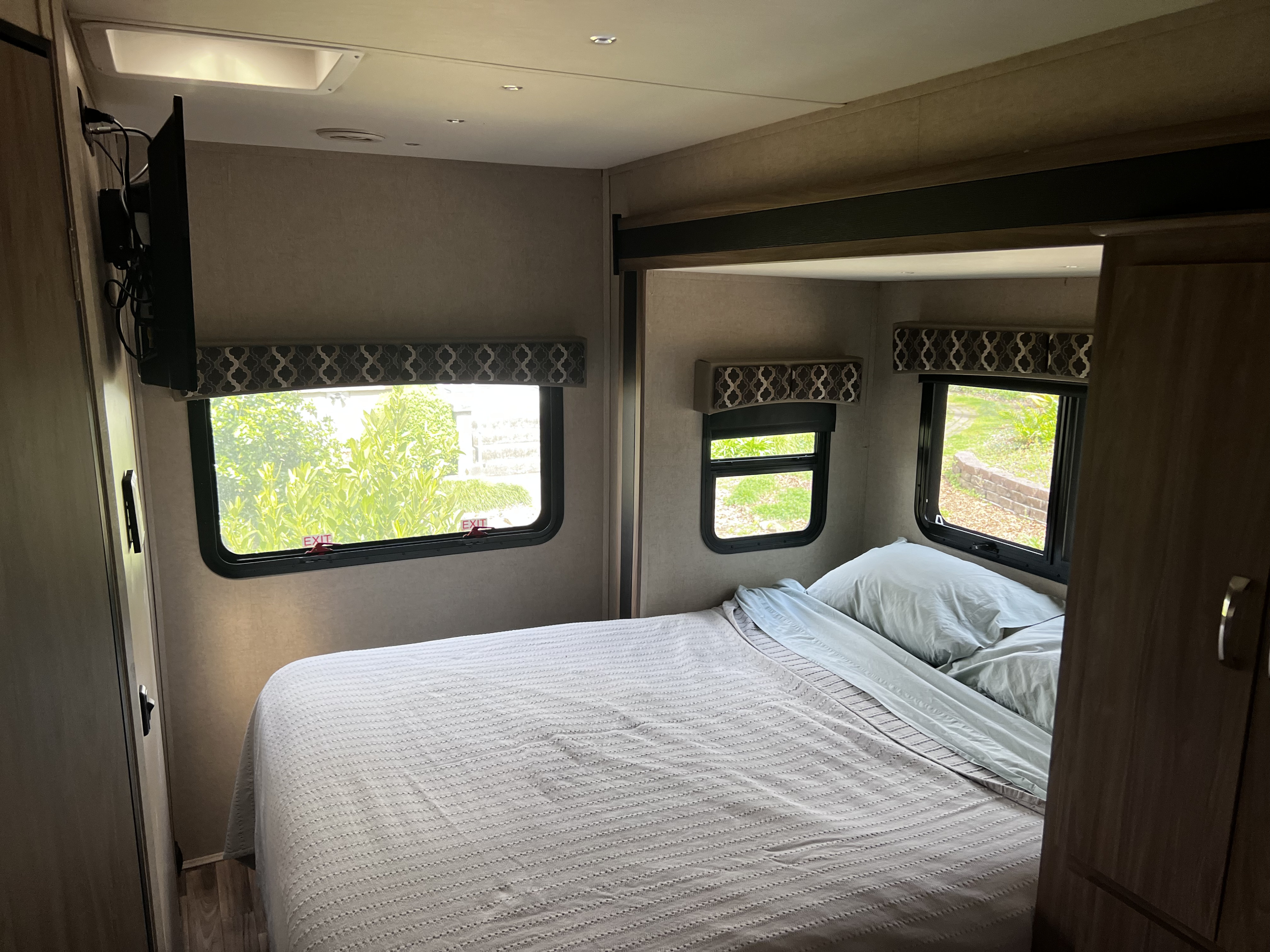 Comfortable RV rental travel trailer bedroom with bed, windows showcasing green views, and a wall-mounted TV.. Isata 3 2017